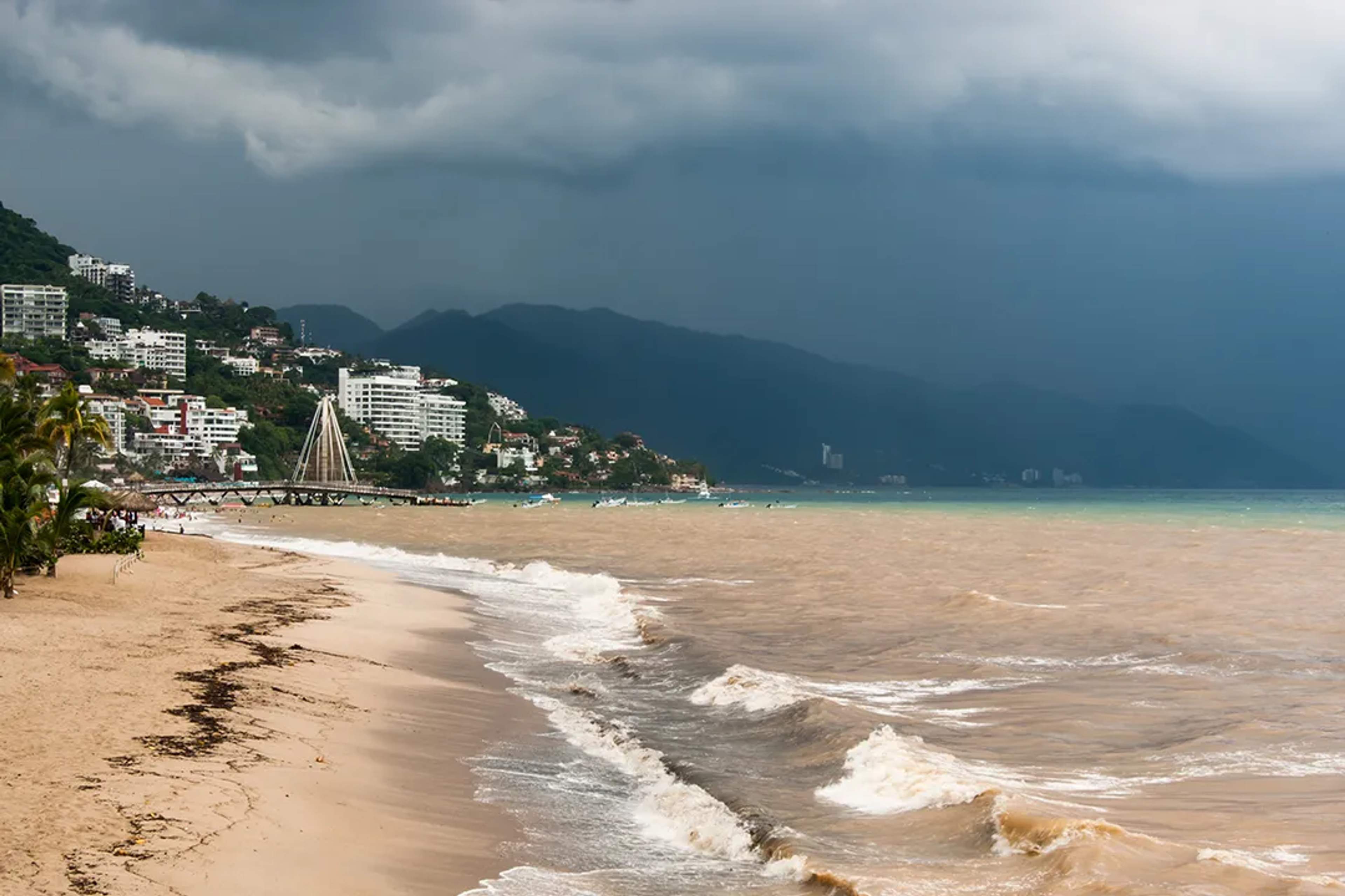 Nubes de tormenta cubren el muelle de Los Muertos y olas golpean la orilla turbia en Vallarta.