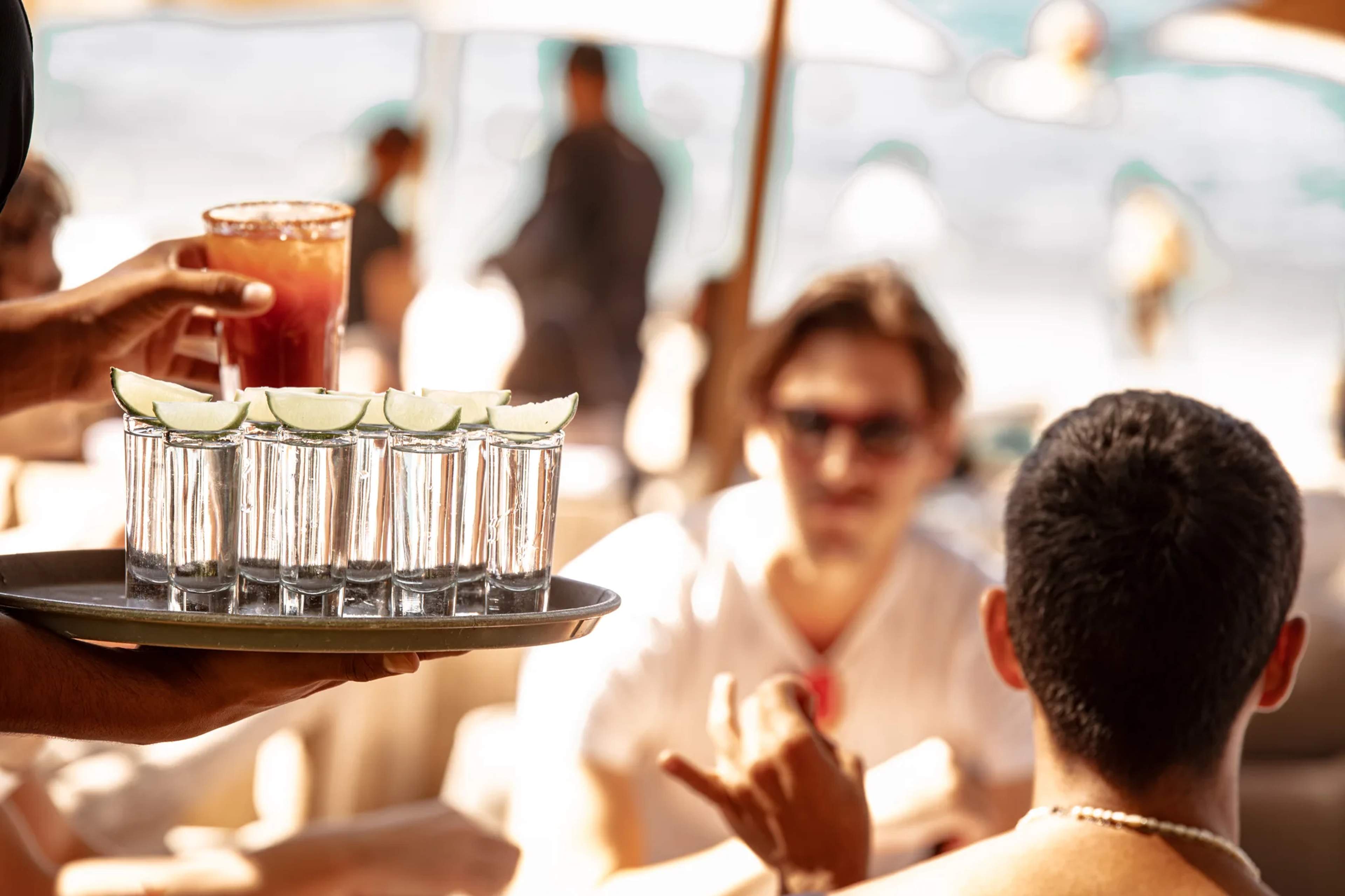 A server offers tequila shots with lime wedges to guests at a sun-soaked beachside bar in Banderas Bay.