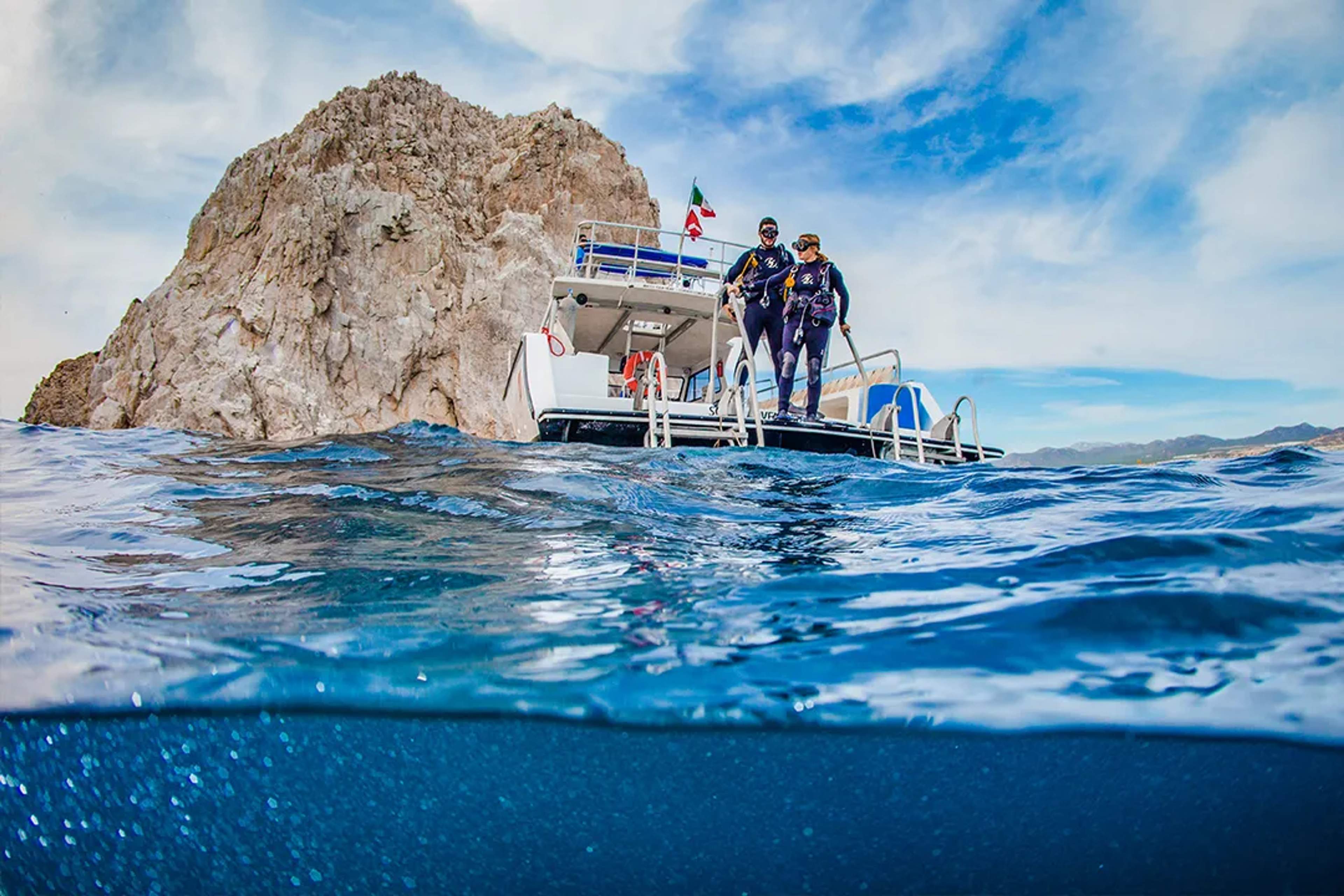 Divers prepare to jump from a boat into the clear blue waters near rocky cliffs in Mexico.