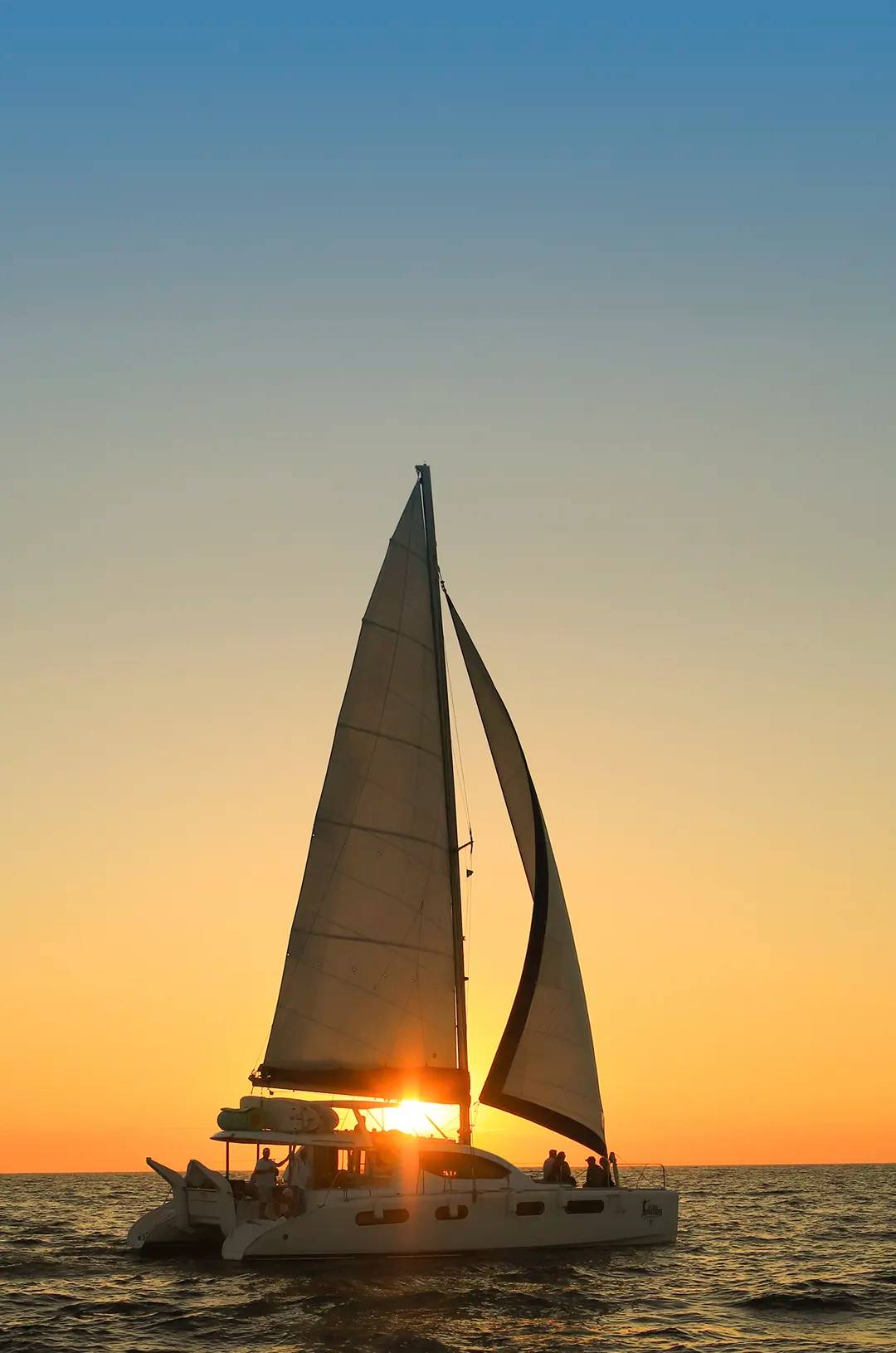 A sailboat sails on the ocean during sunset in Puerto Vallarta, with the golden sun peeking through the sails.