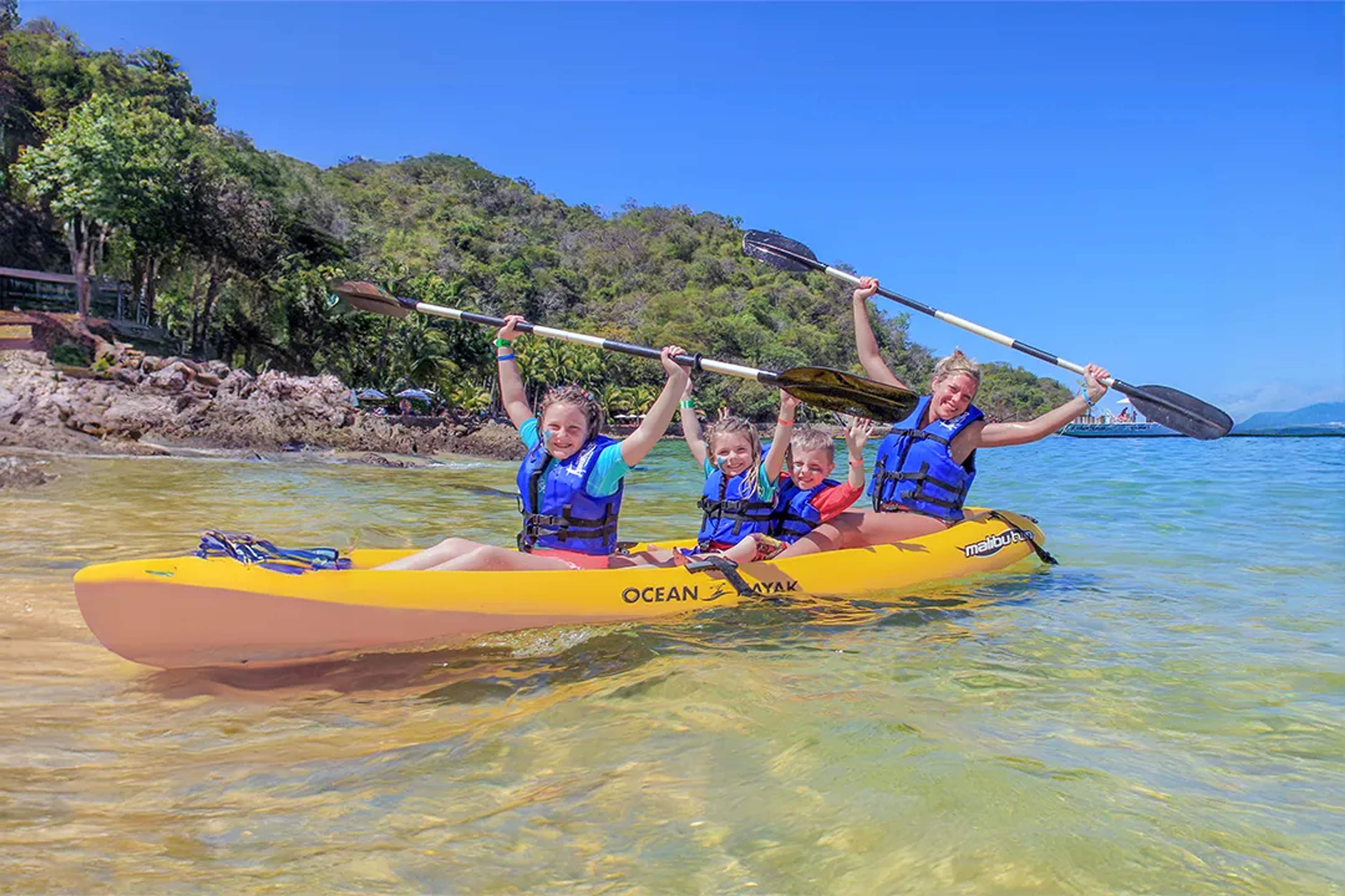Familia feliz en kayak con chalecos salvavidas, rodeada de selva y cielo azul.