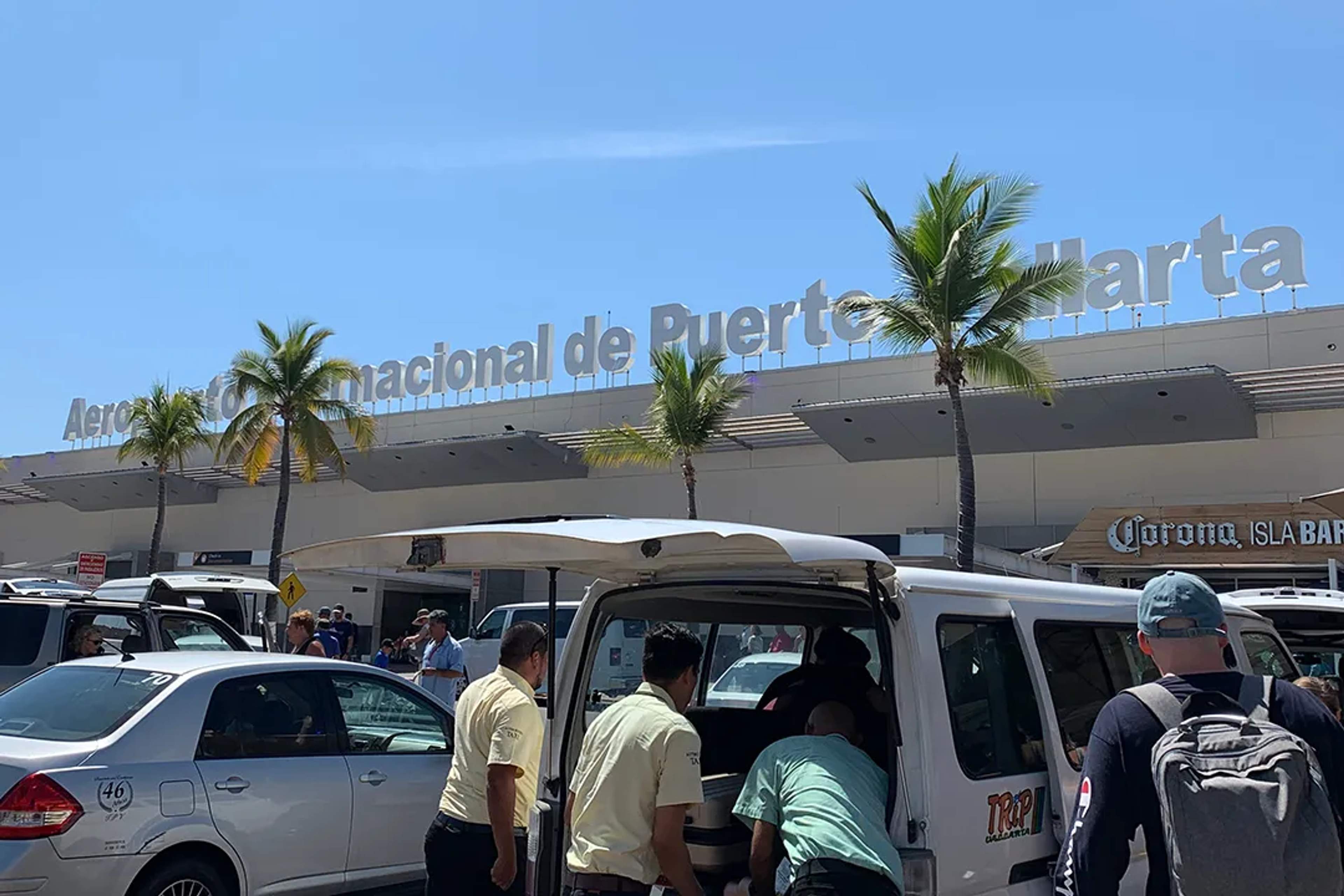 Viajeros llegan al Aeropuerto de Puerto Vallarta bajo un cielo soleado y palmeras.