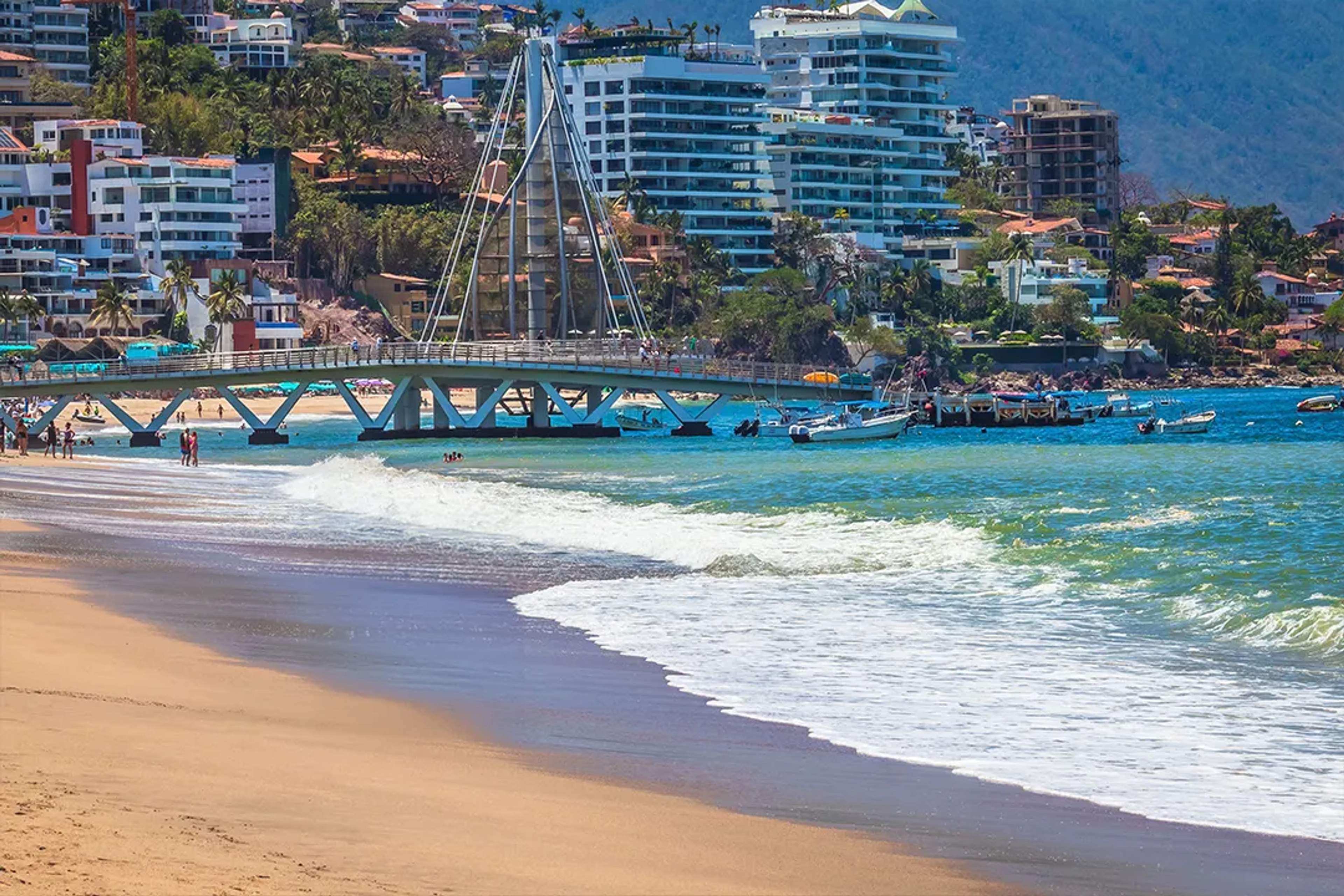 El muelle de Los Muertos se alza sobre el mar turquesa en Vallarta, con lanchas y bañistas.