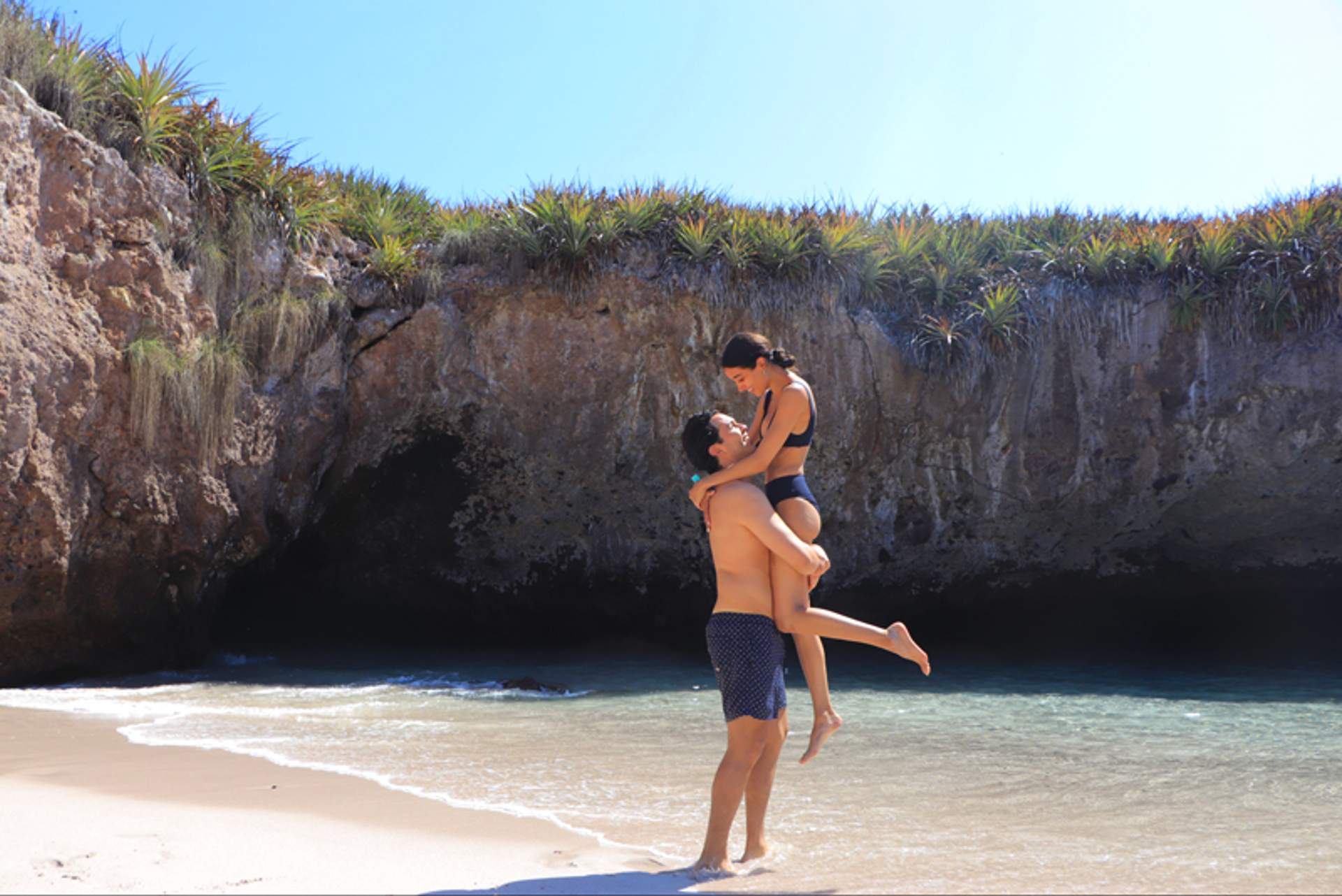 A couple enjoying a romantic moment on the sandy Hidden Beach, surrounded by cliffs and clear waters in Marieta Islands, Mexico.