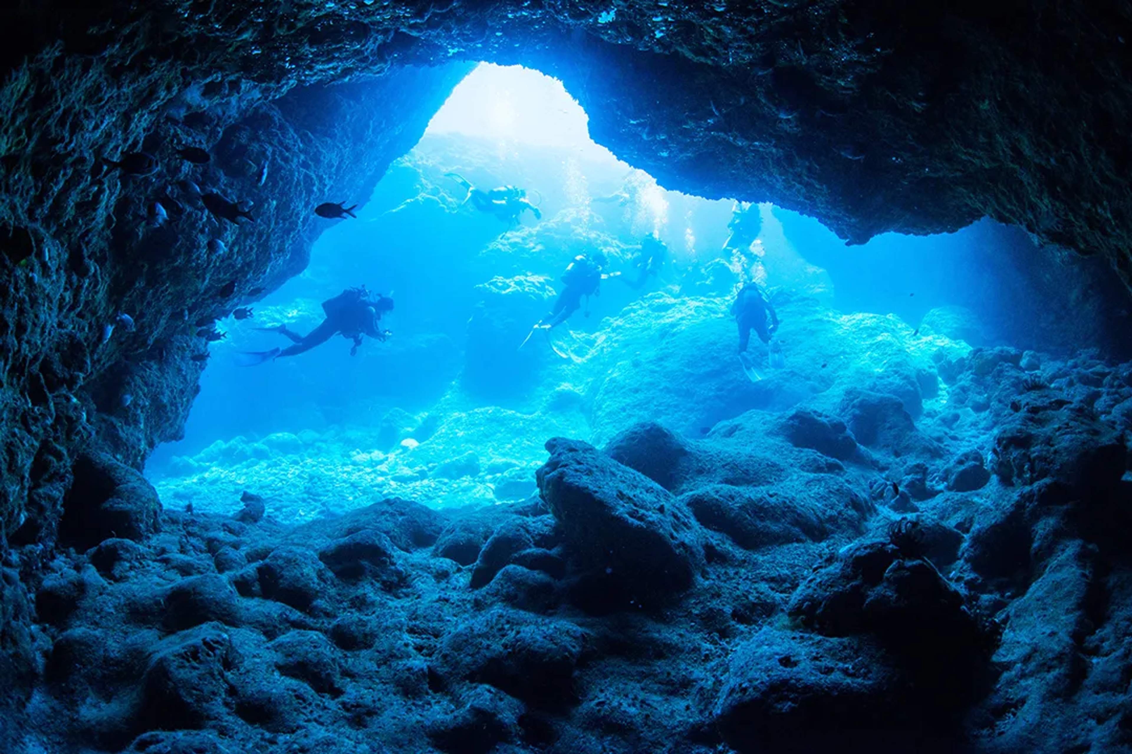 Divers explore a stunning underwater cave, illuminated by sunlight filtering through the entrance.
