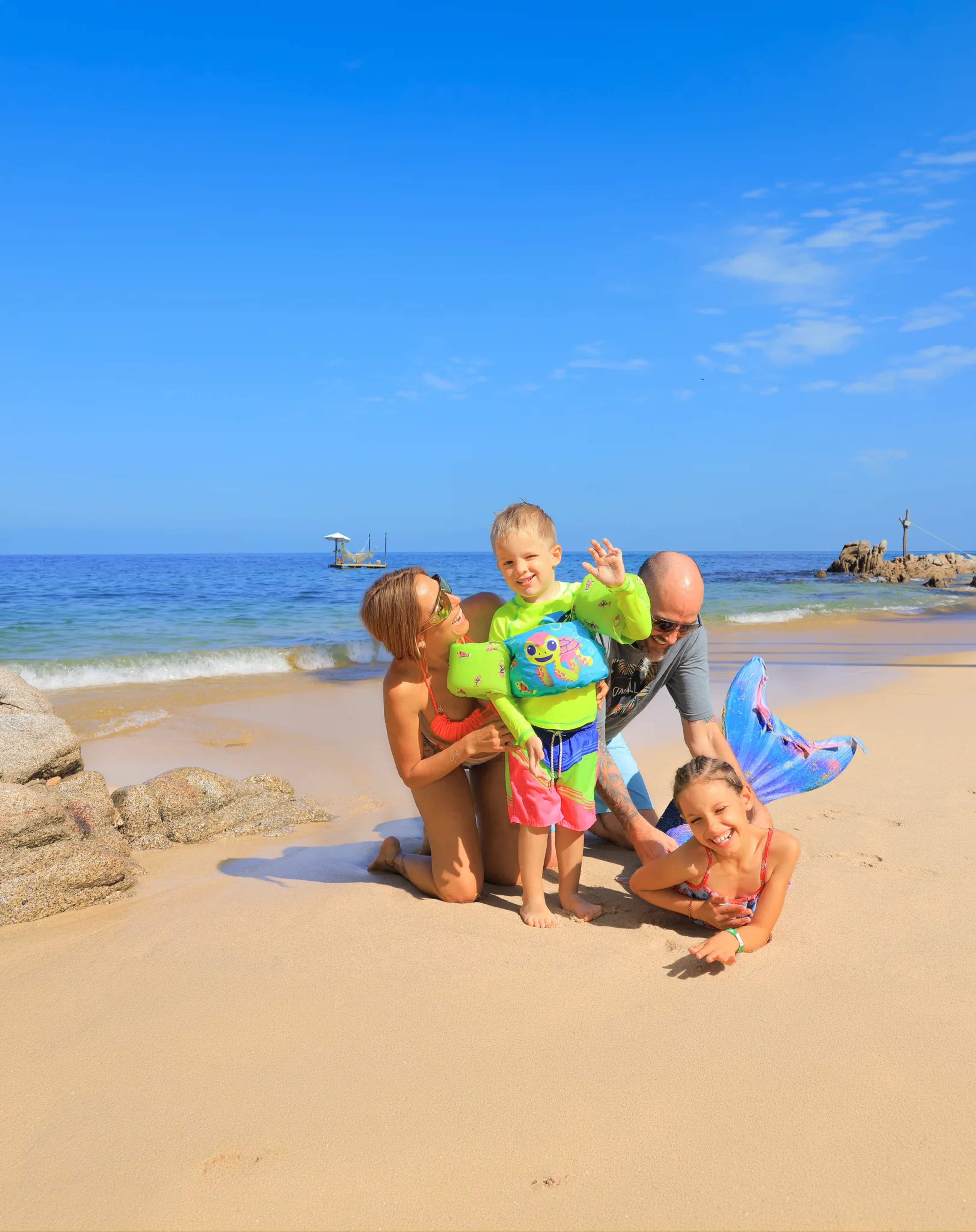 Familia de cuatro personas disfrutando un día soleado en la playa de Las Caletas con niños en trajes de baño coloridos.