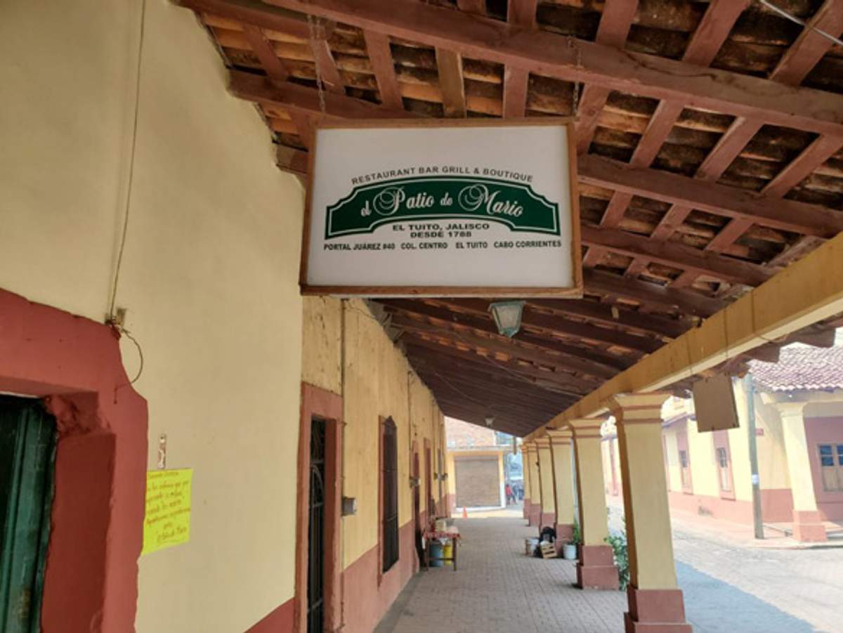 Un letrero de "El Patio de Mario" cuelga bajo un pasillo cubierto con paredes amarillas y bordes rojos.