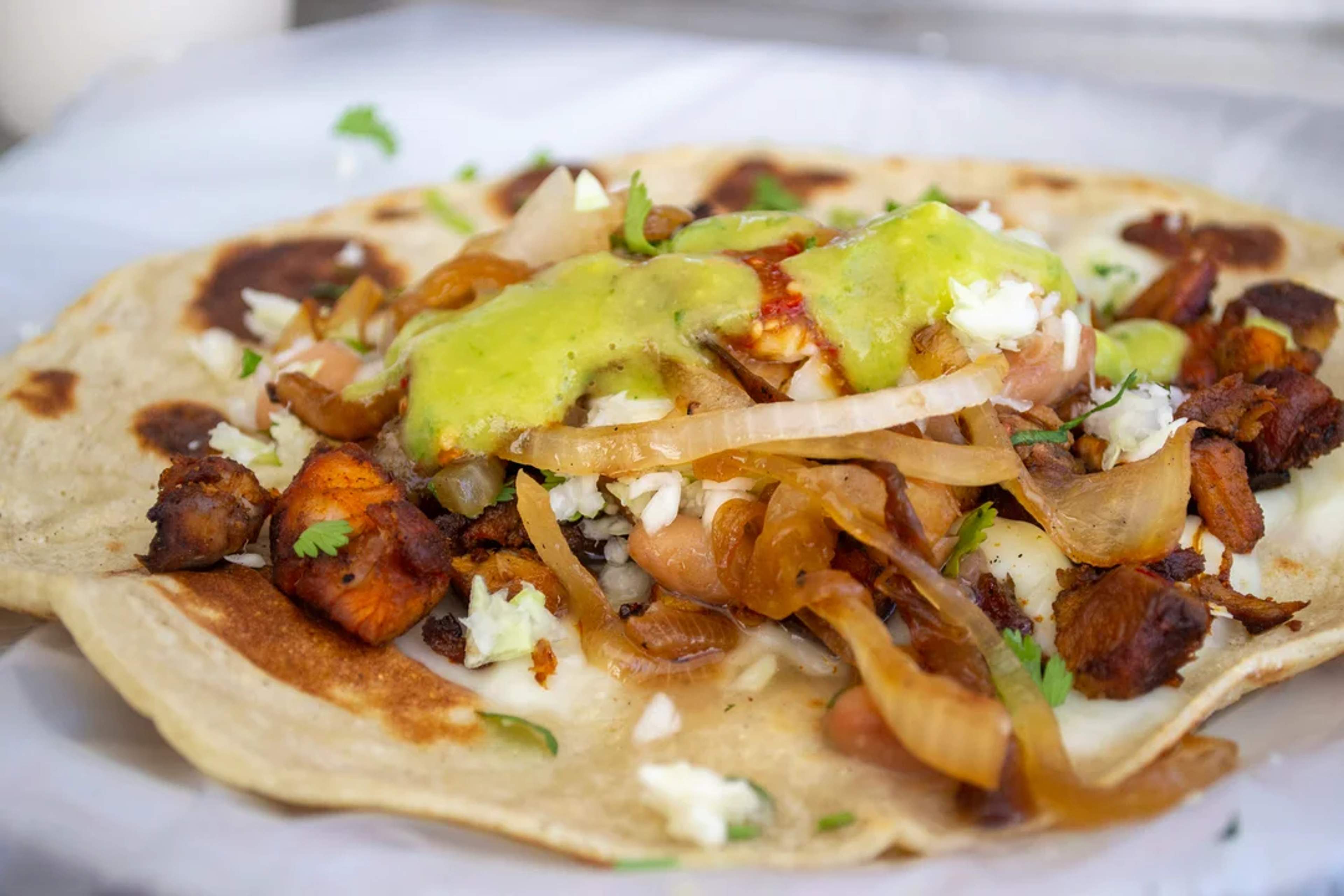 Taco al pastor con cebolla caramelizada, queso, salsa verde y tortilla dorada al comal.