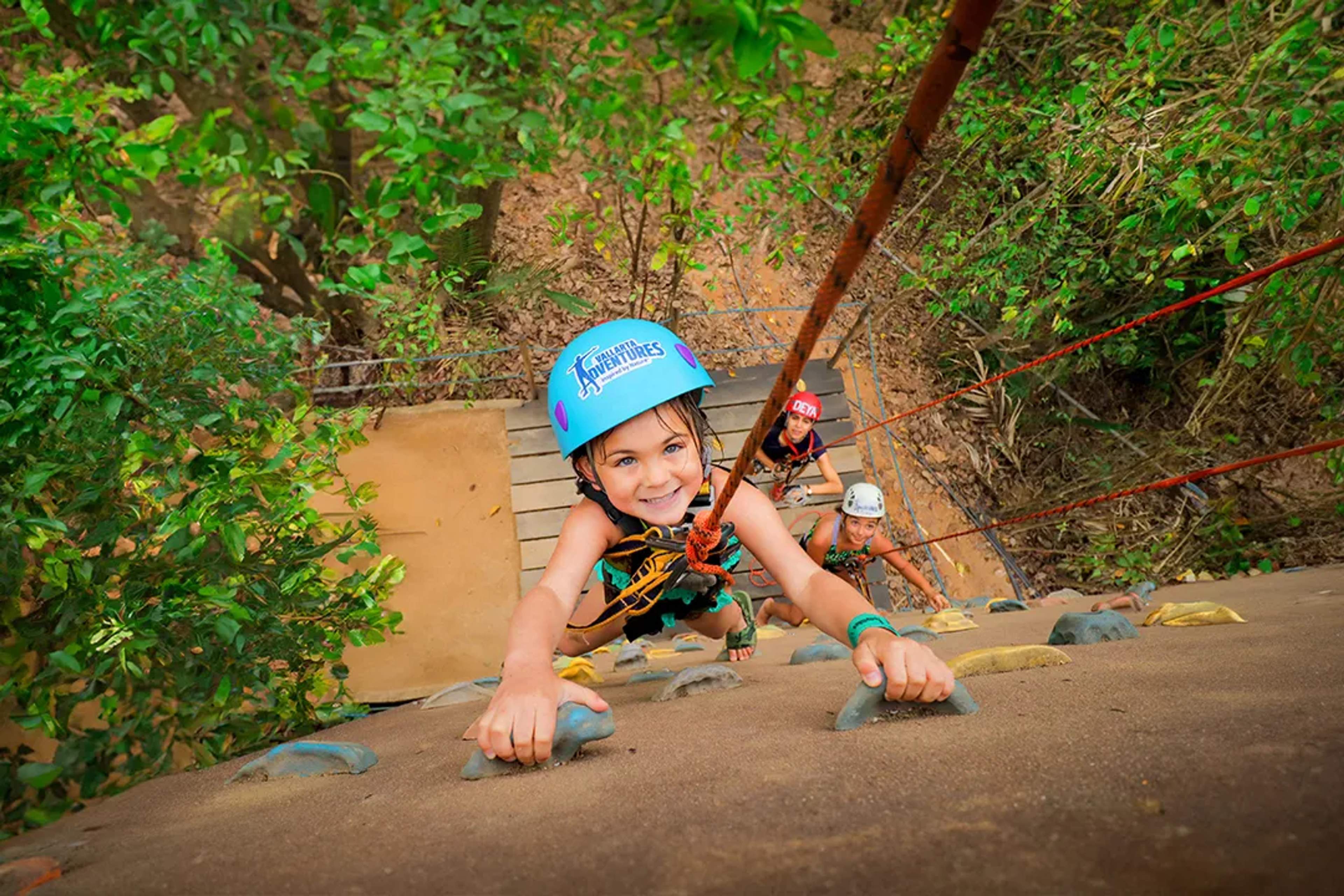 Child climbing a jungle rock wall with safety gear during a fun, family-friendly adventure experience in Mexico