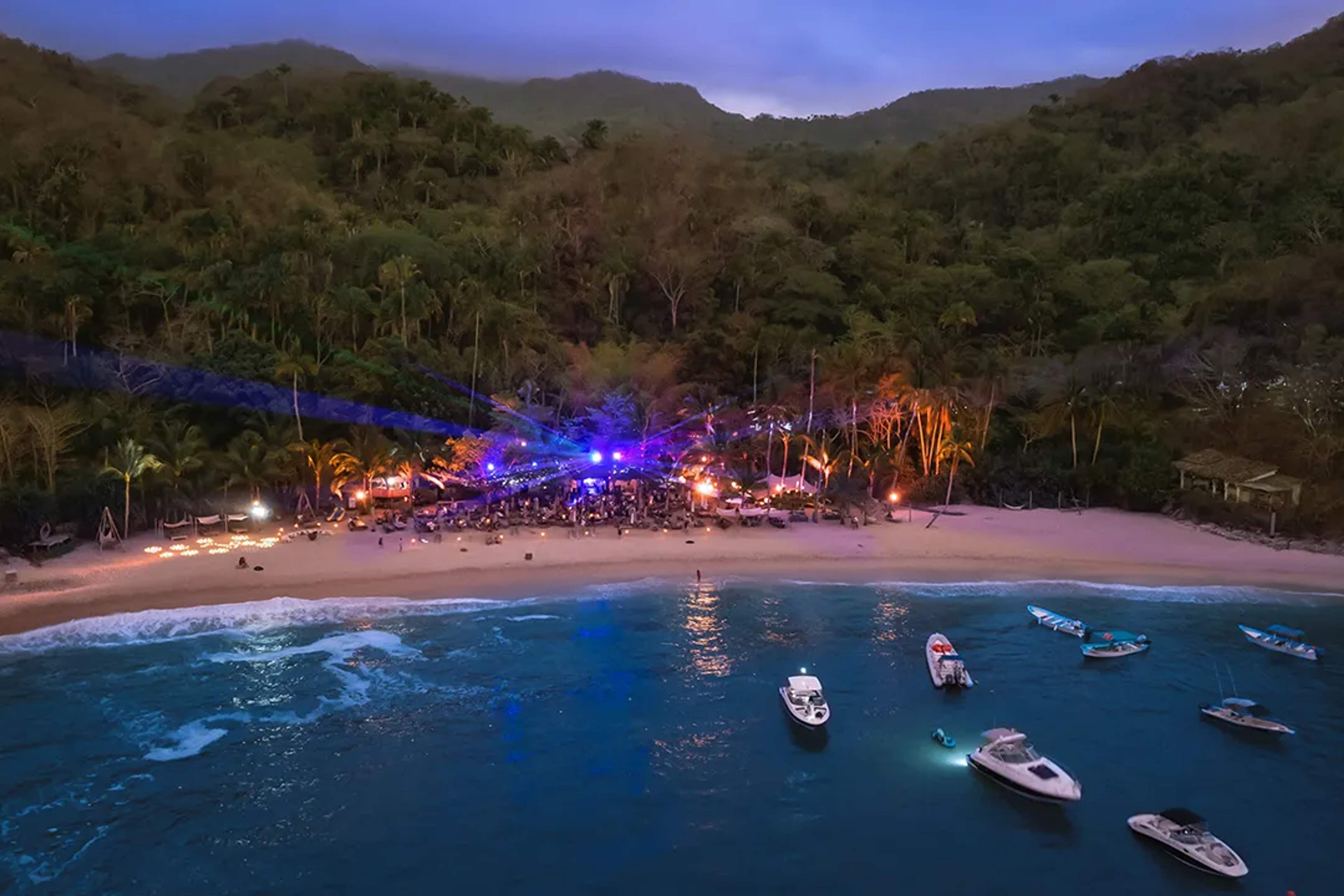 Secluded Majahuitas beach party with boats, lights, and jungle backdrop at sunset.