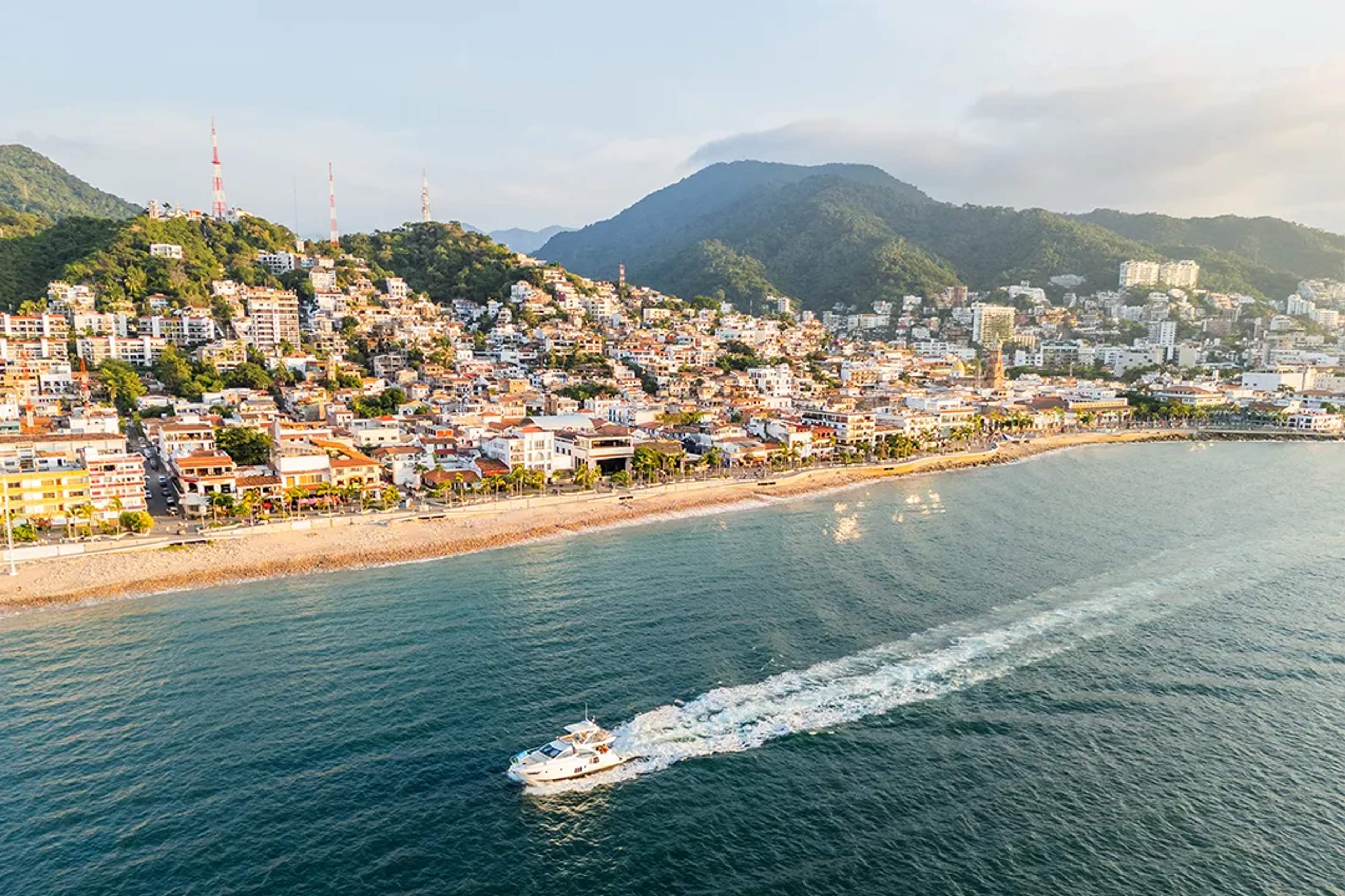 Aerial view of Puerto Vallarta’s coastline with a boat cruising past the beach and hills.