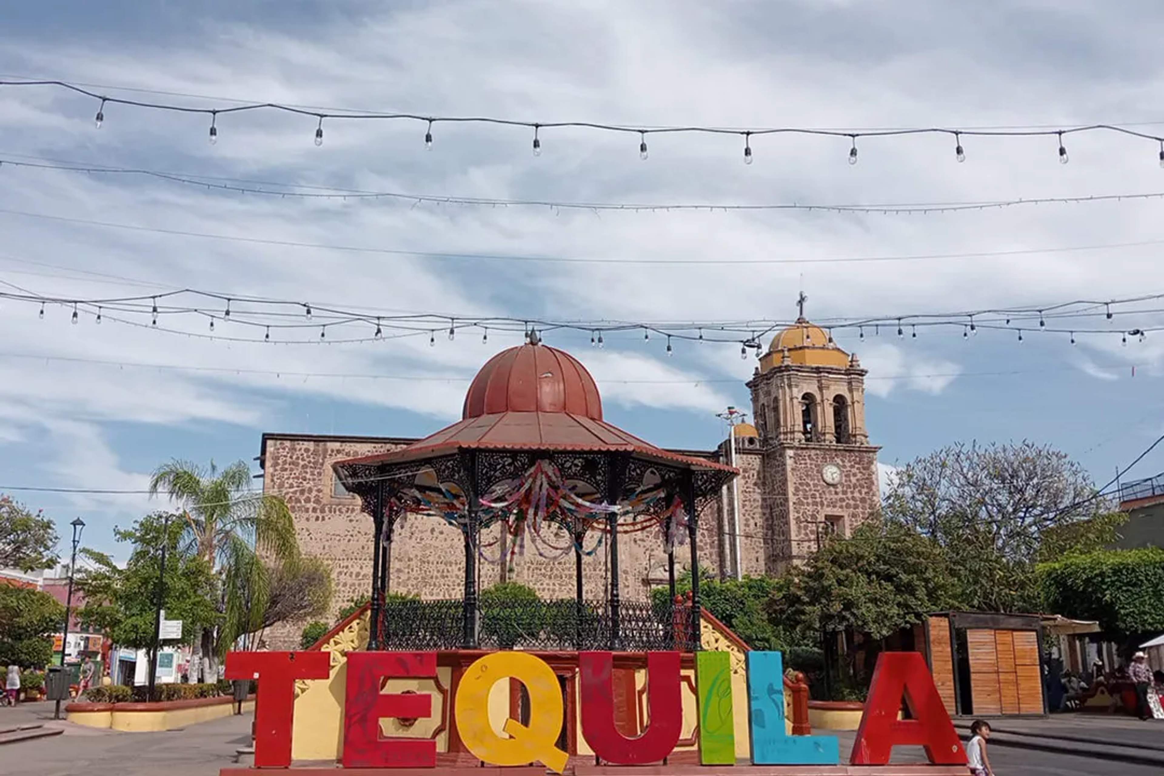 Colorful Tequila sign and kiosk in the town plaza, with the historic church tower behind.