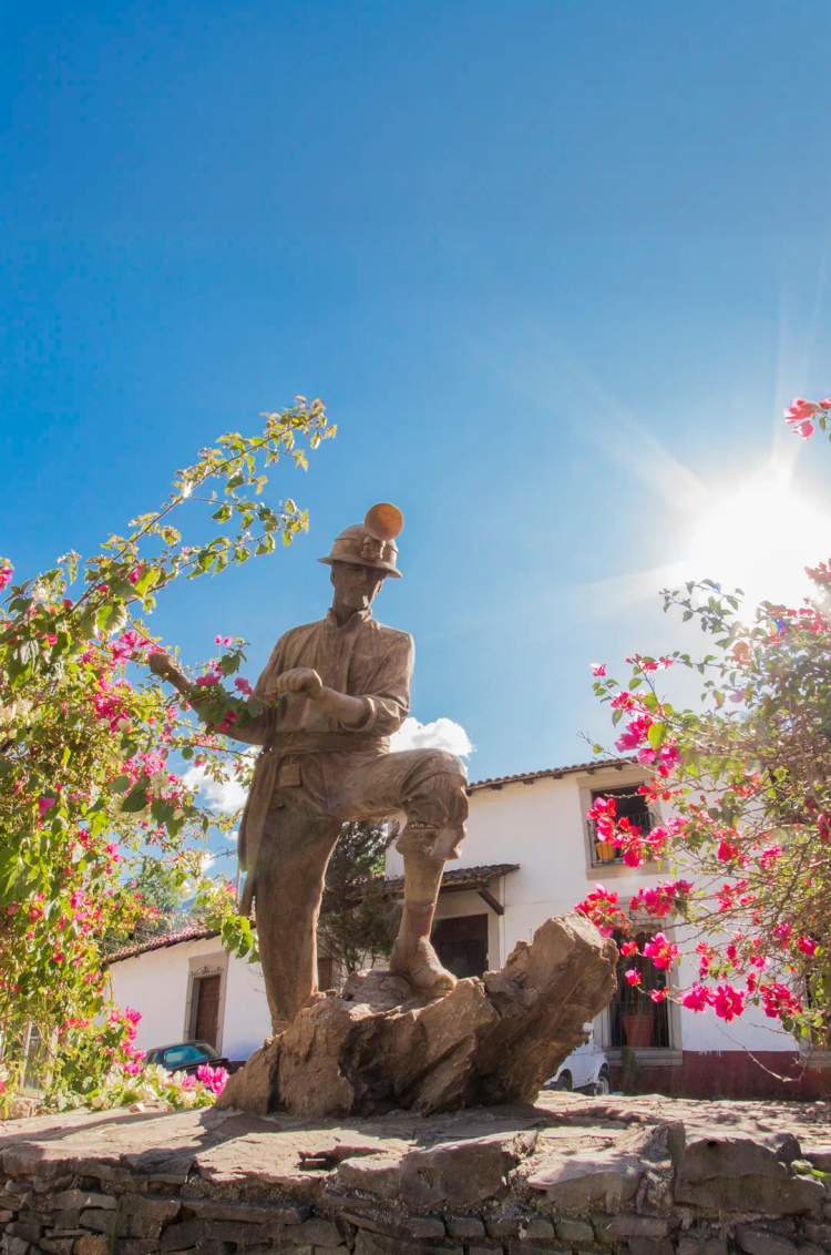 Miner statue surrounded by blooming flowers in San Sebastian del Oeste.