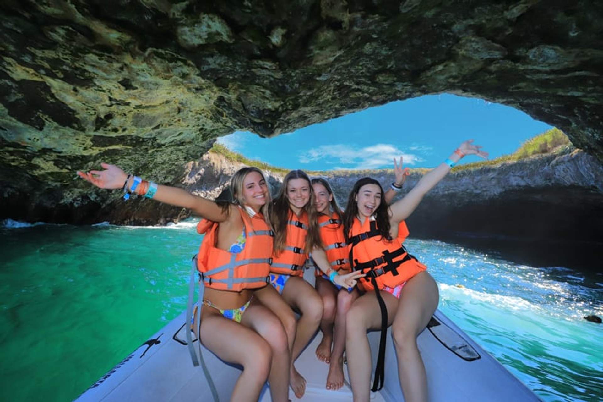 Four women in life jackets smiling and posing on a boat at the entrance of Hidden Beach, Marieta Islands, Mexico.