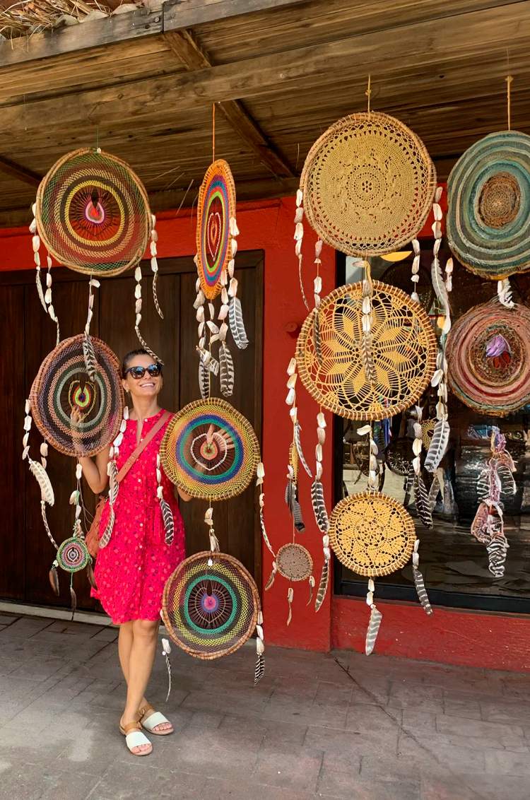 Woman smiling among colorful handmade dreamcatchers in Sayulita, Mexico, as part of a Sayulita shopping tour.
