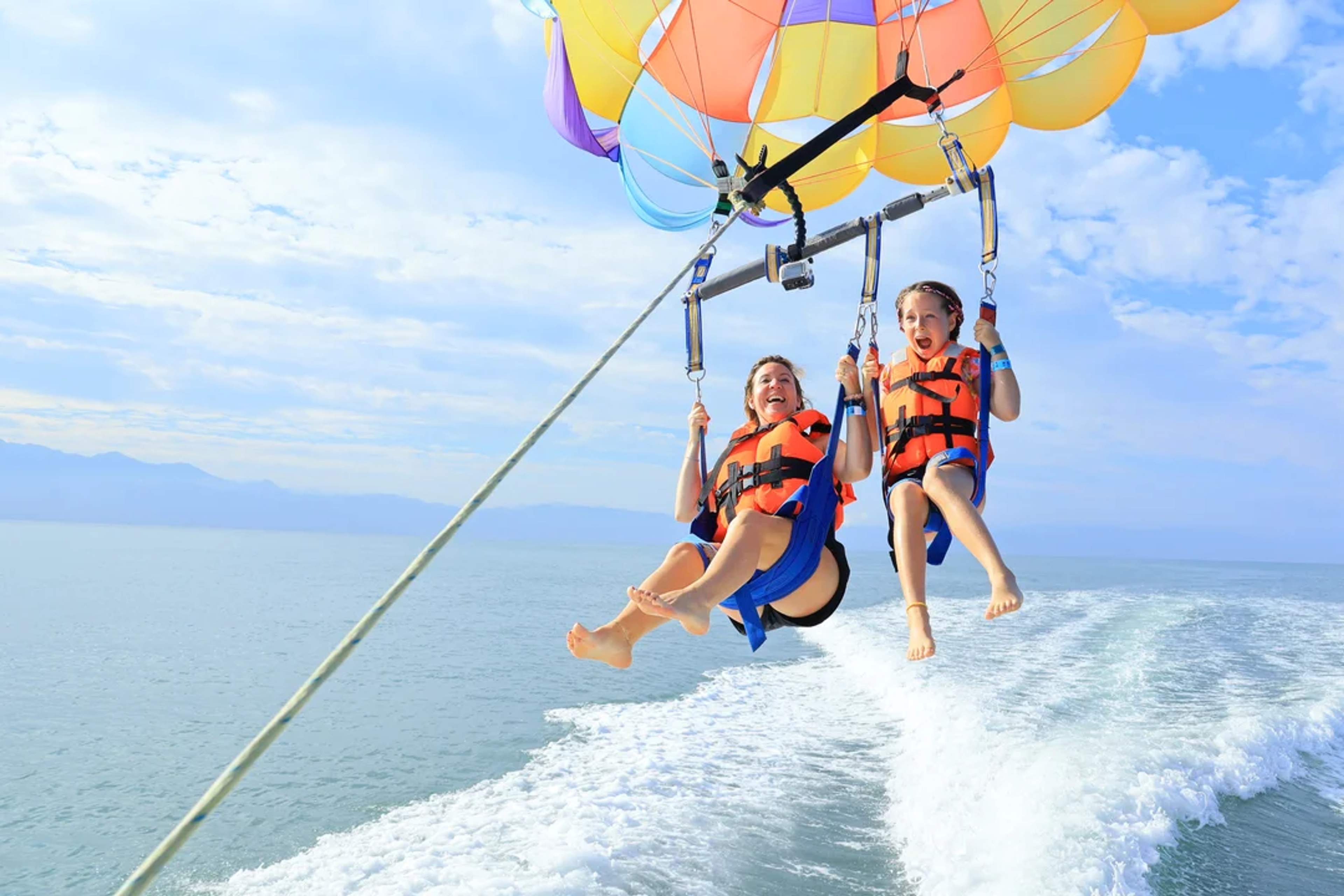Madre e hija disfrutan del paracaídas sobre el mar, sonriendo con emoción y aventura.