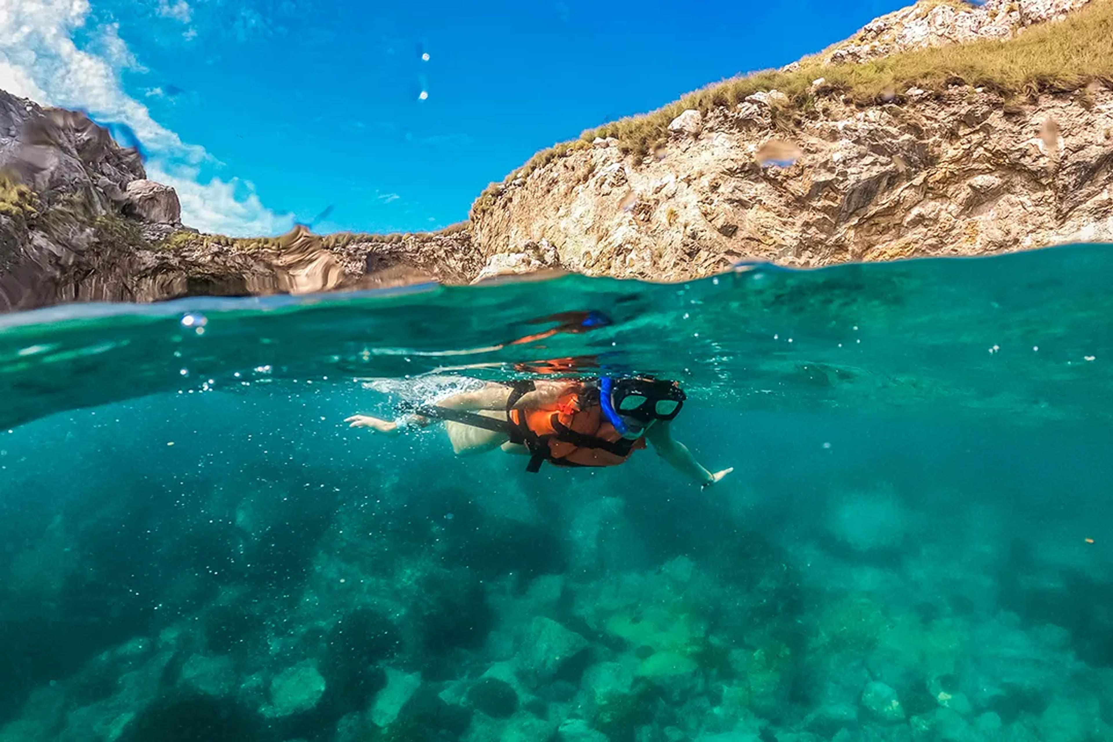 A snorkeler with life vest explores crystal-clear waters and rocky reefs in Marietas Islands.