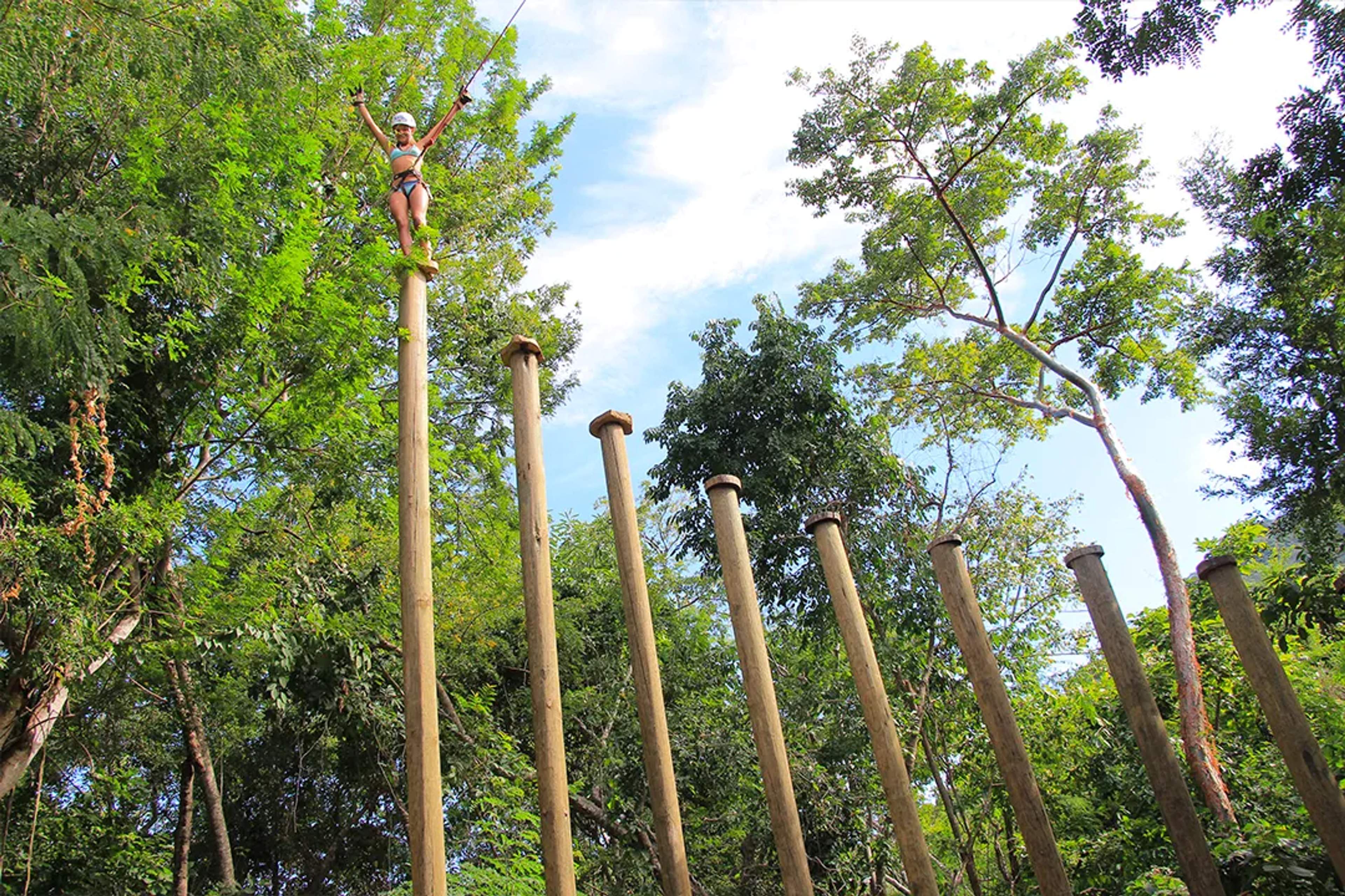 Person climbing tall wooden poles in the jungle during the Extreme Adventure tour in Puerto Vallarta  (100 caracteres exactos)