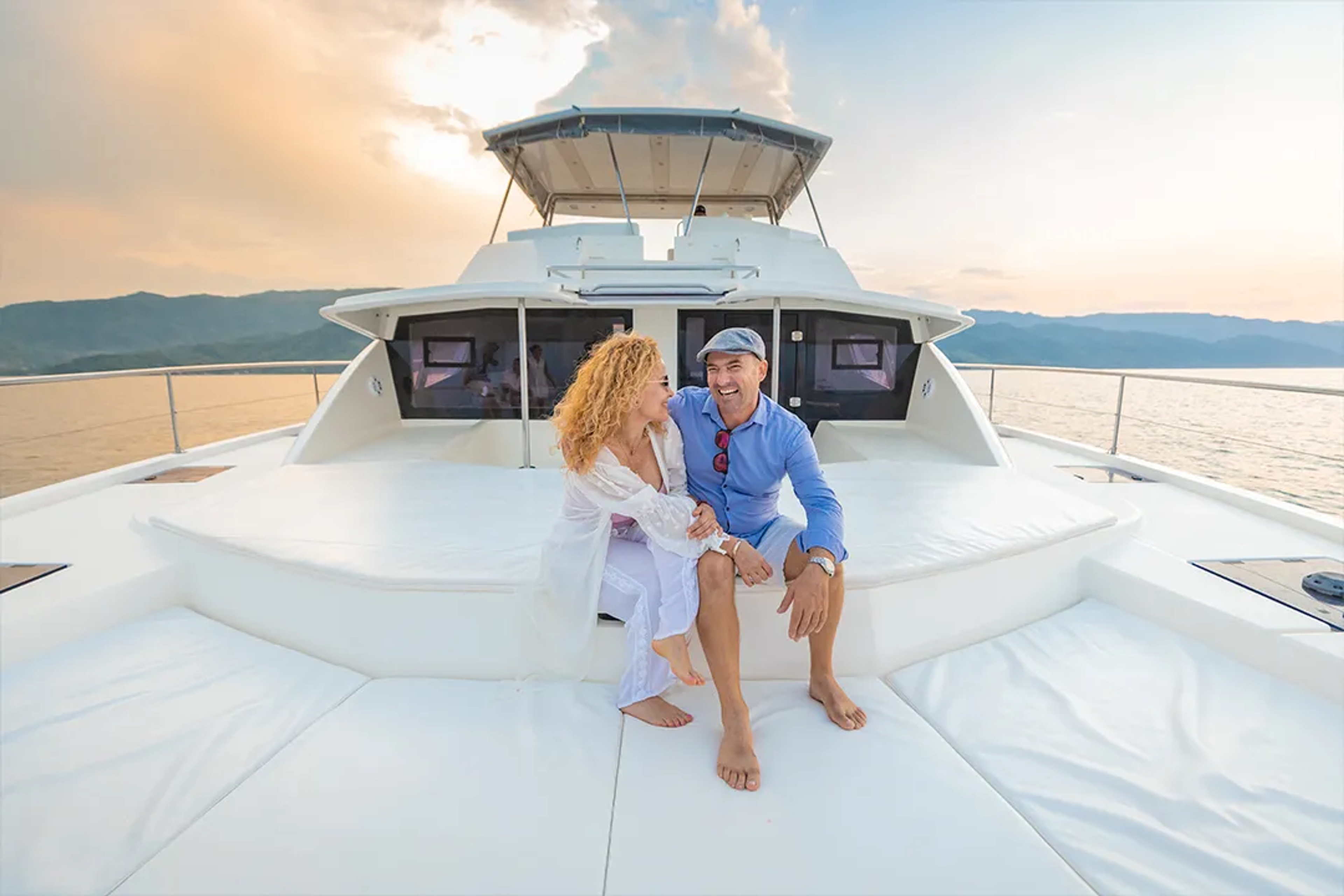 A smiling couple enjoys a relaxing moment on a yacht at sunset.