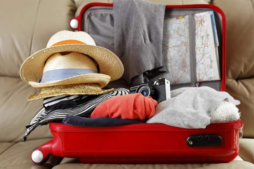 Open suitcase packed with clothes, hat, camera, and map, preparing for a summer vacation or city getaway