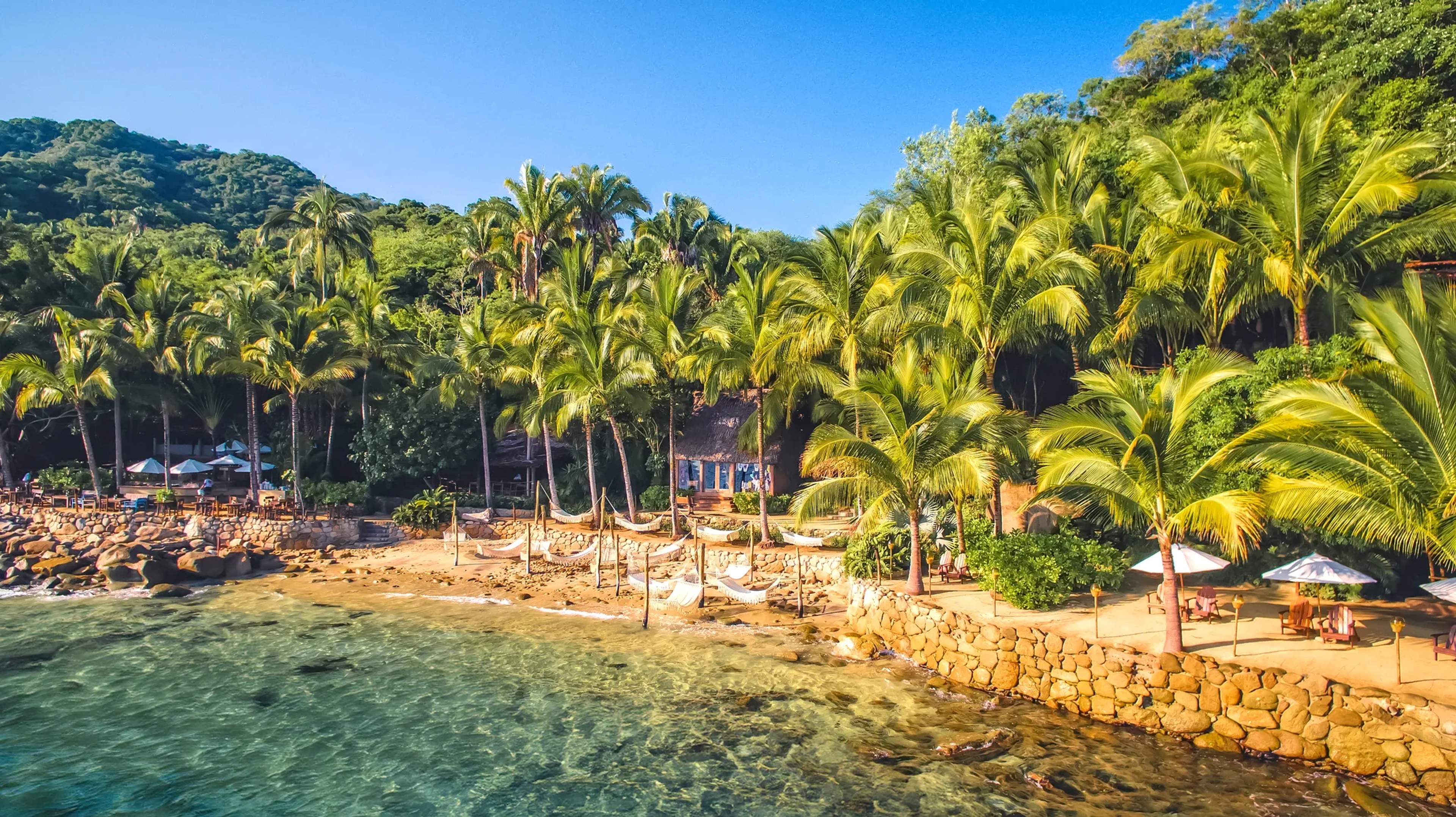 Secluded beach cove at Las Caletas with clear turquoise water, golden sand, palm trees, and rustic wooden beachfront