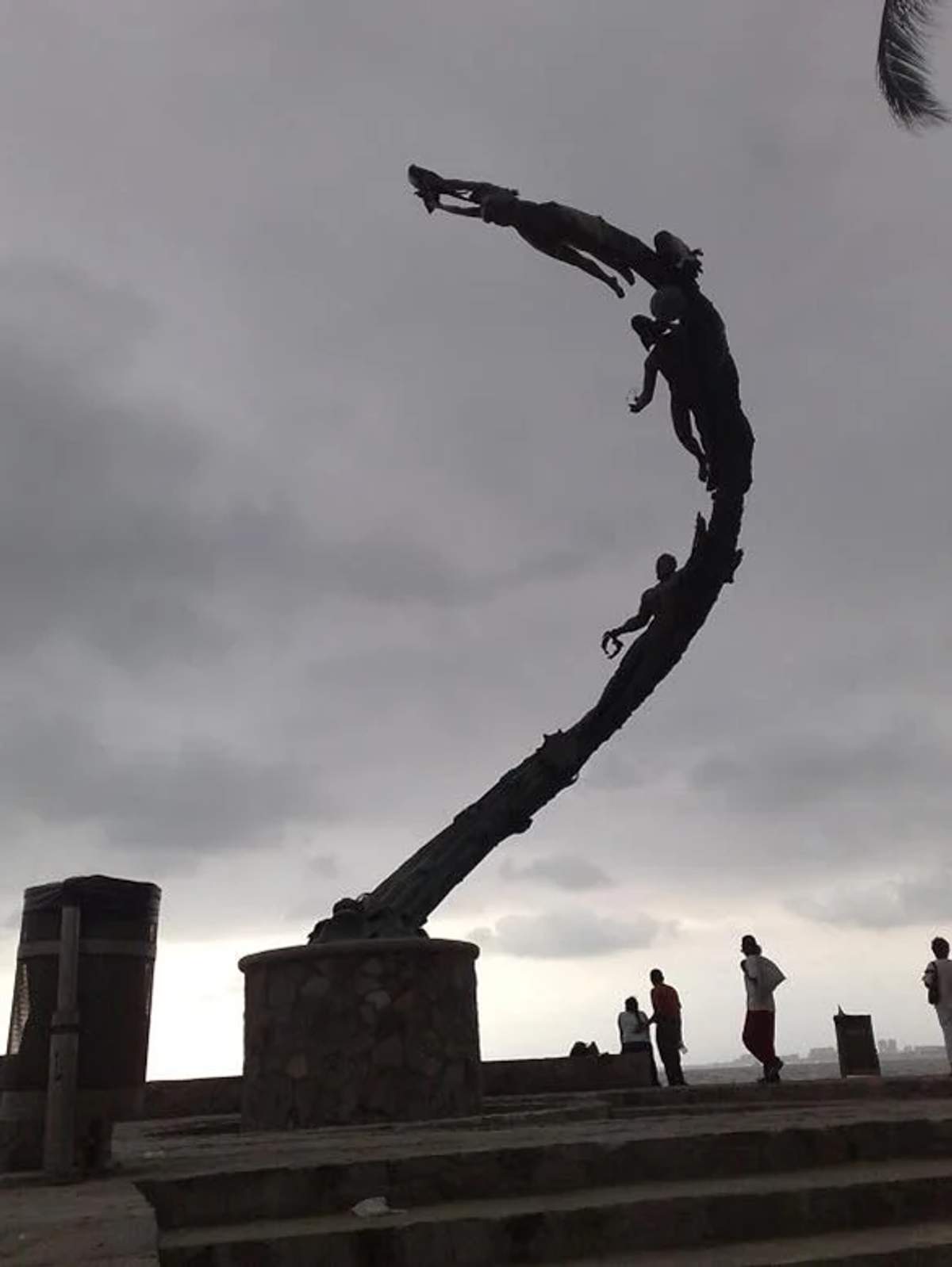 Escultura "El Milenio" en Puerto Vallarta, muestra figuras humanas ascendiendo en espiral bajo un cielo nublado.