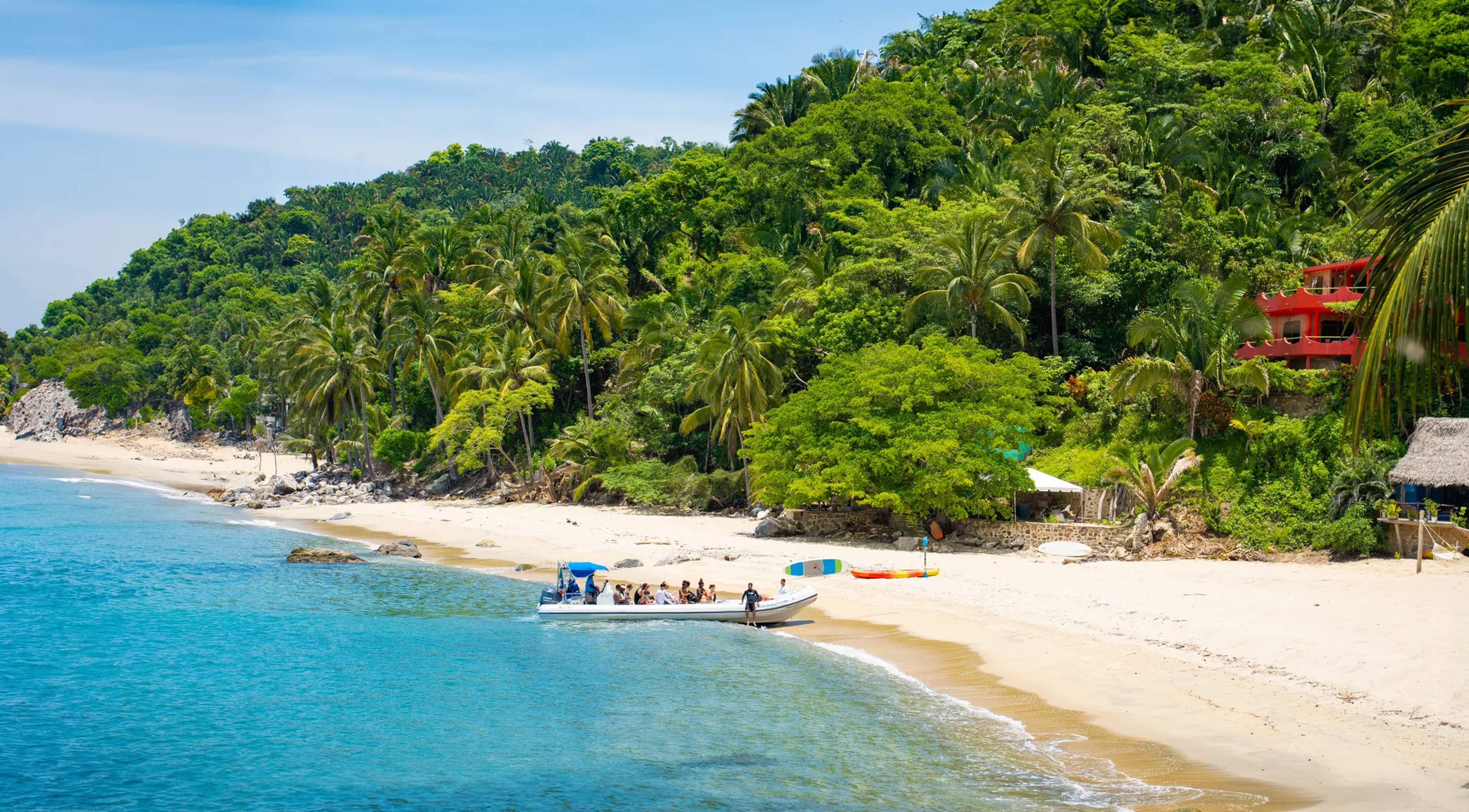 A tour boat pulls ashore on a pristine white-sand beach backed by dense tropical jungle on Mexico's Pacific coast