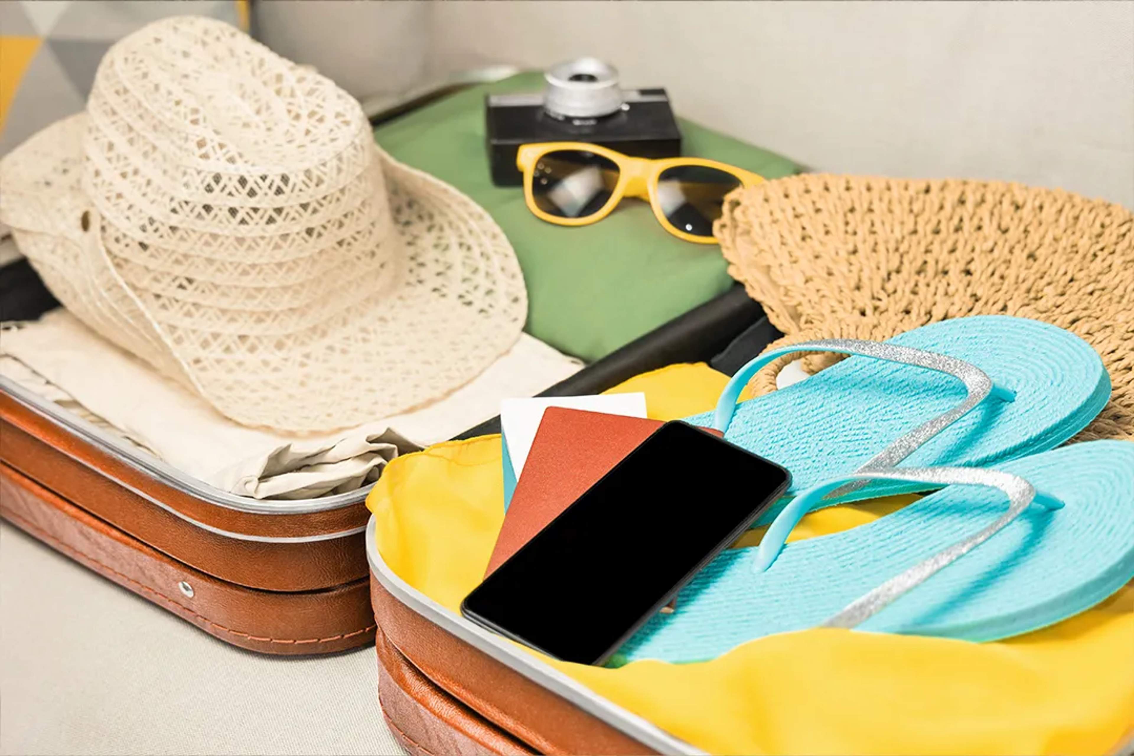 Empacando esenciales de playa para verano con sandalias, lentes, sombrero y accesorios en maleta abierta