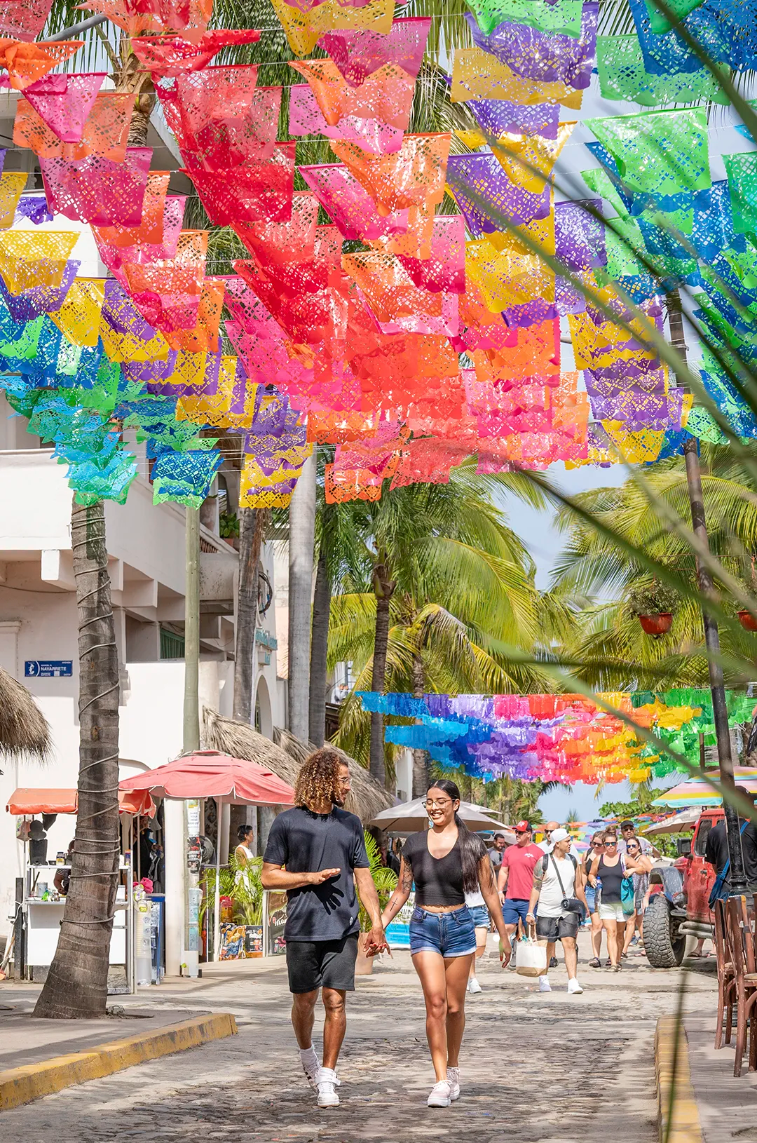 Couple walking under colorful papel picado in Sayulita's bustling street, during a walking tour with Vallarta Adventures.