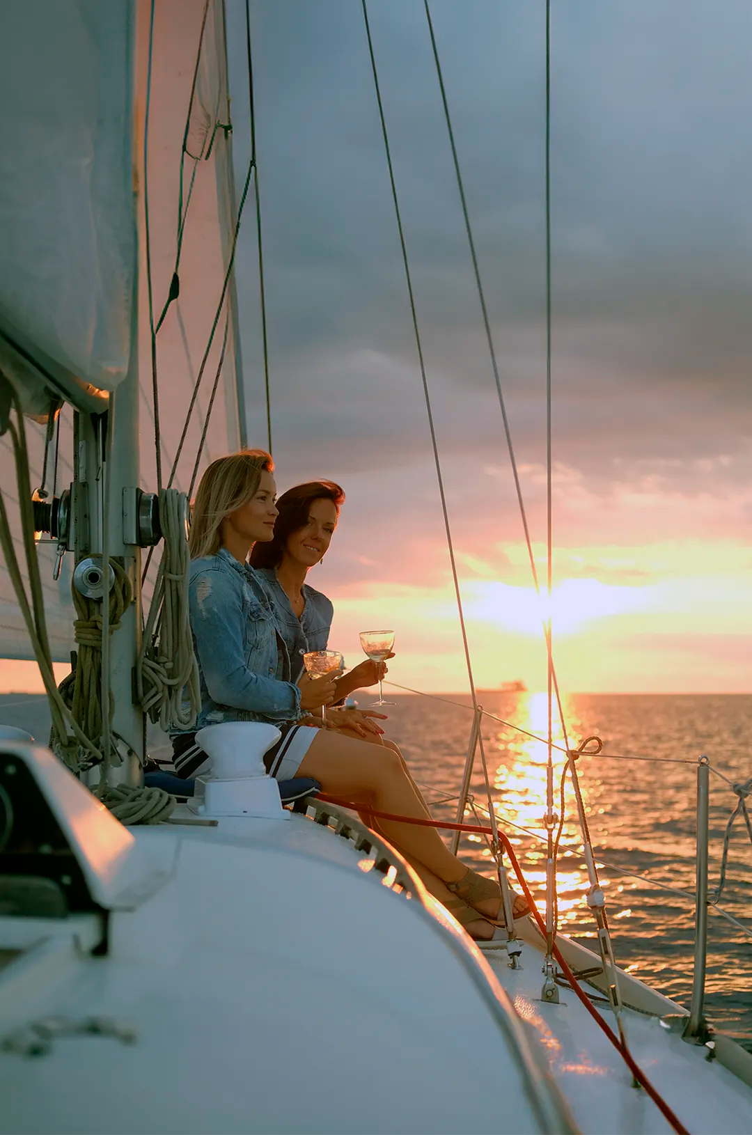 Amigas en un velero al atardecer en Puerto Vallarta, disfrutando de bebidas y la vista del sol poniéndose en el mar.