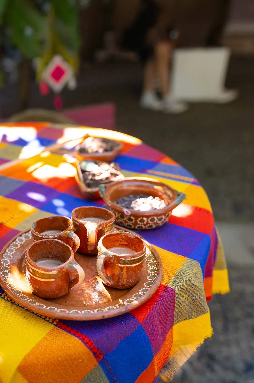 Traditional Mexican grinding stone called metate, cacao seeds, and a cacao drink on a colorful tablecloth.