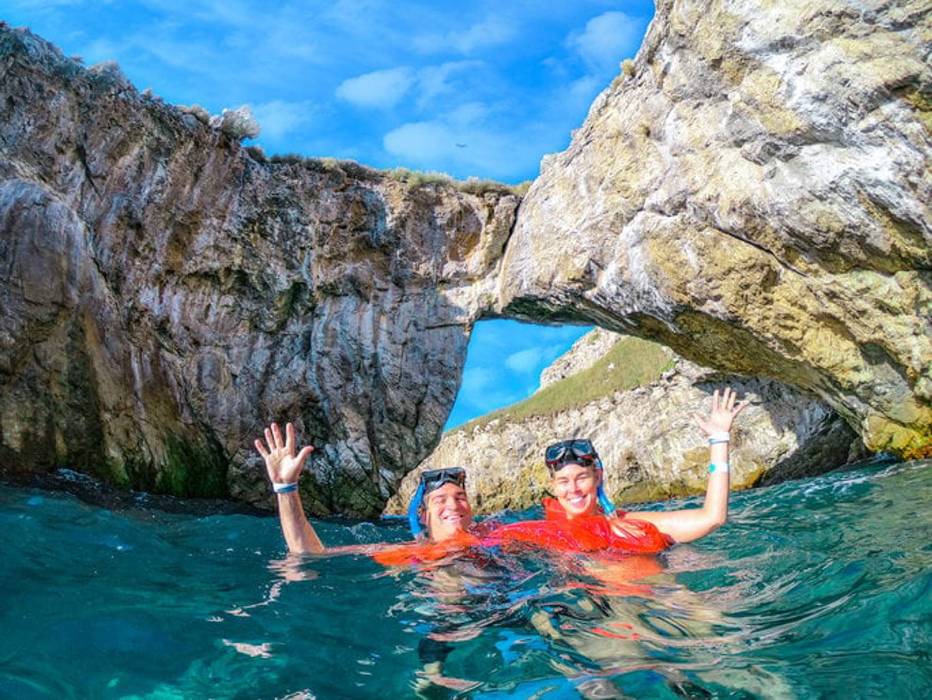 Dos personas haciendo snorkel en Islas Marietas, México, con una formación de arco de roca en el fondo y un cielo azul claro.