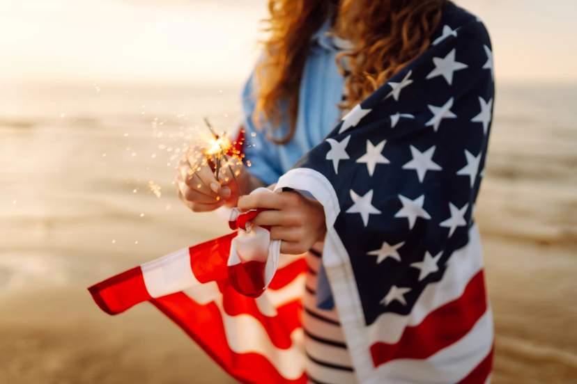 Person holding a sparkler wrapped in an American flag at the beach.