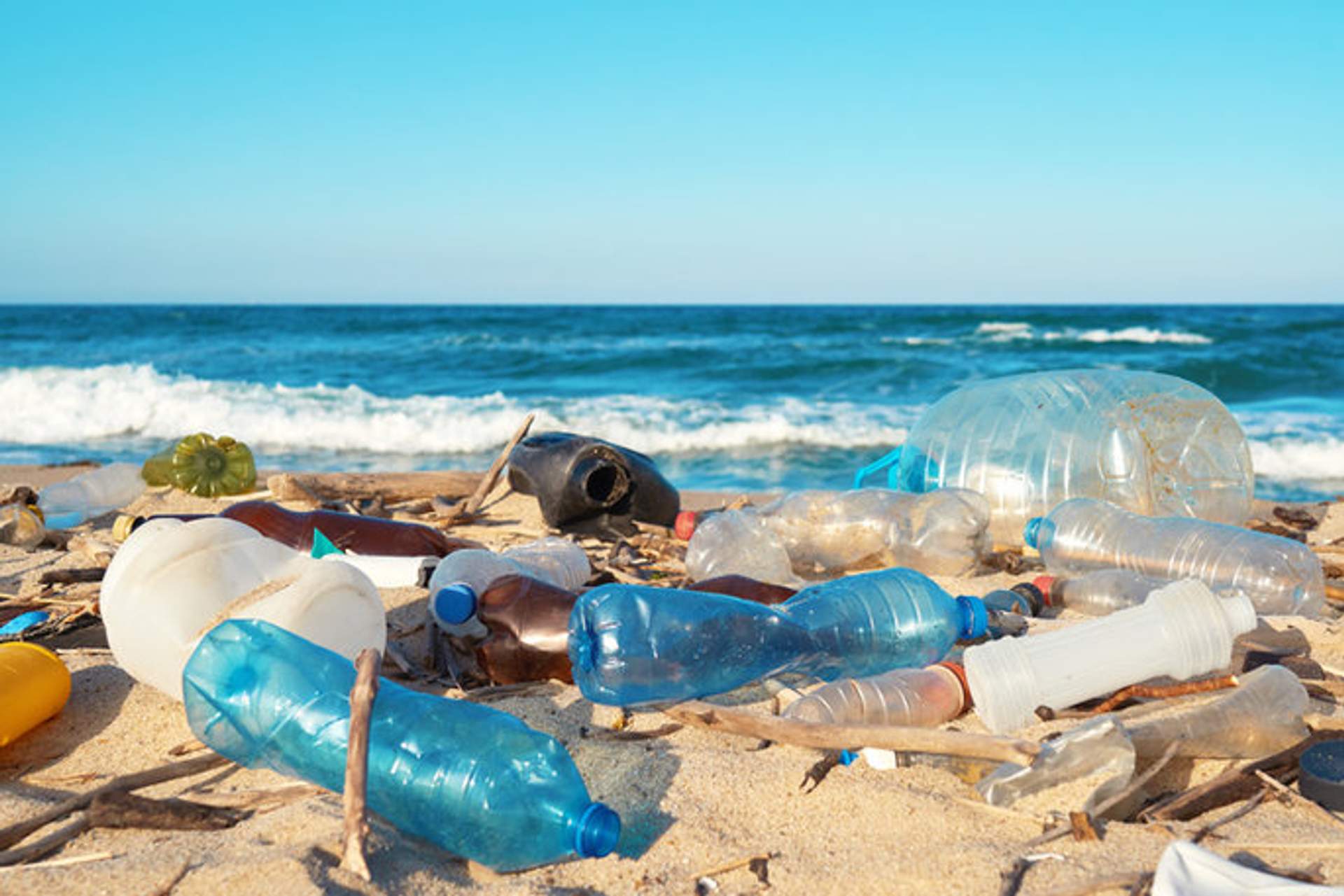 Plastic bottles and trash litter a sandy beach, highlighting the issue of pollution and environmental impact.