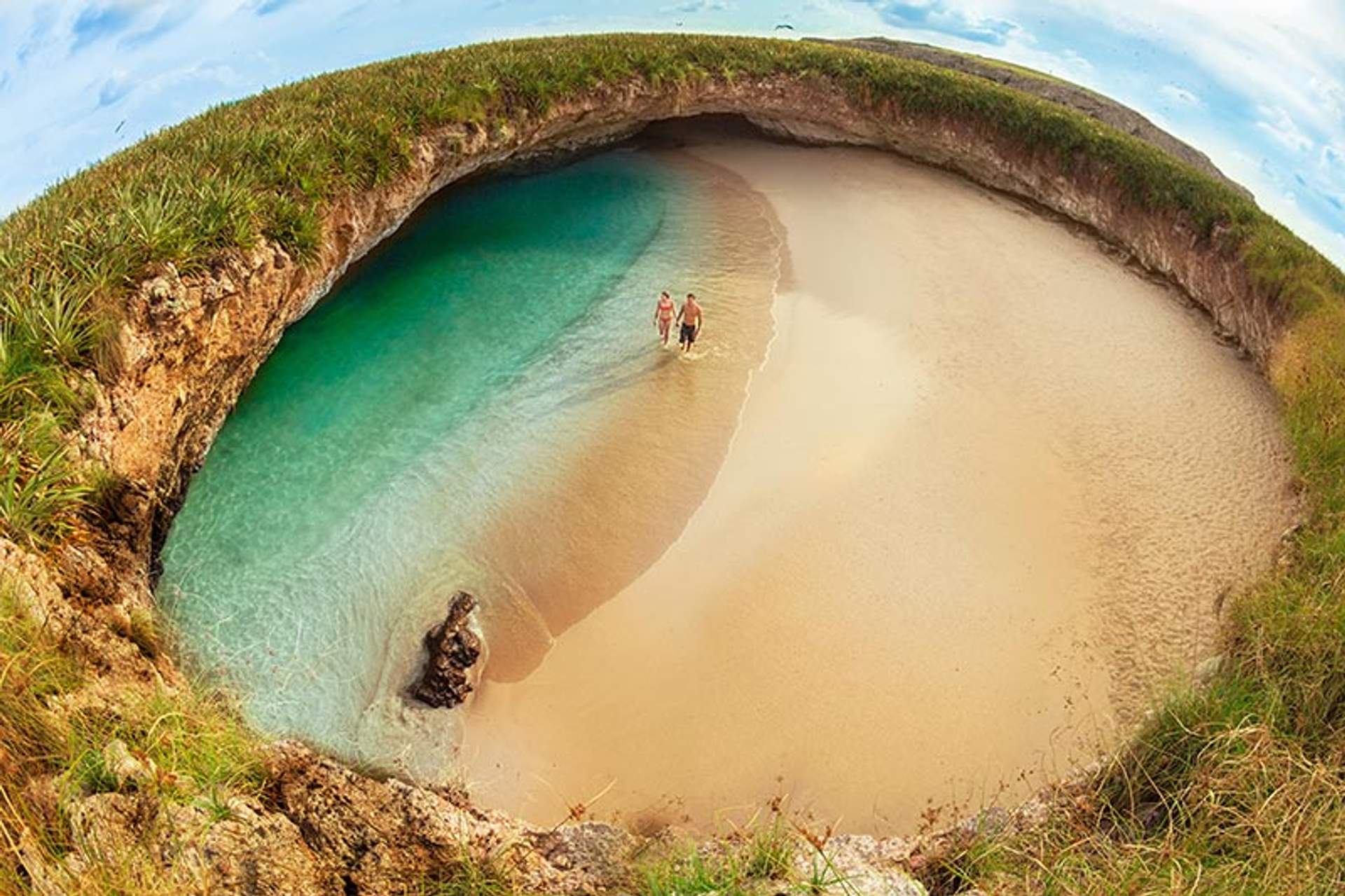 Couple walking on the secluded Hidden Beach with turquoise waters and golden sand, surrounded by lush greenery on Marieta Islands, Mexico.