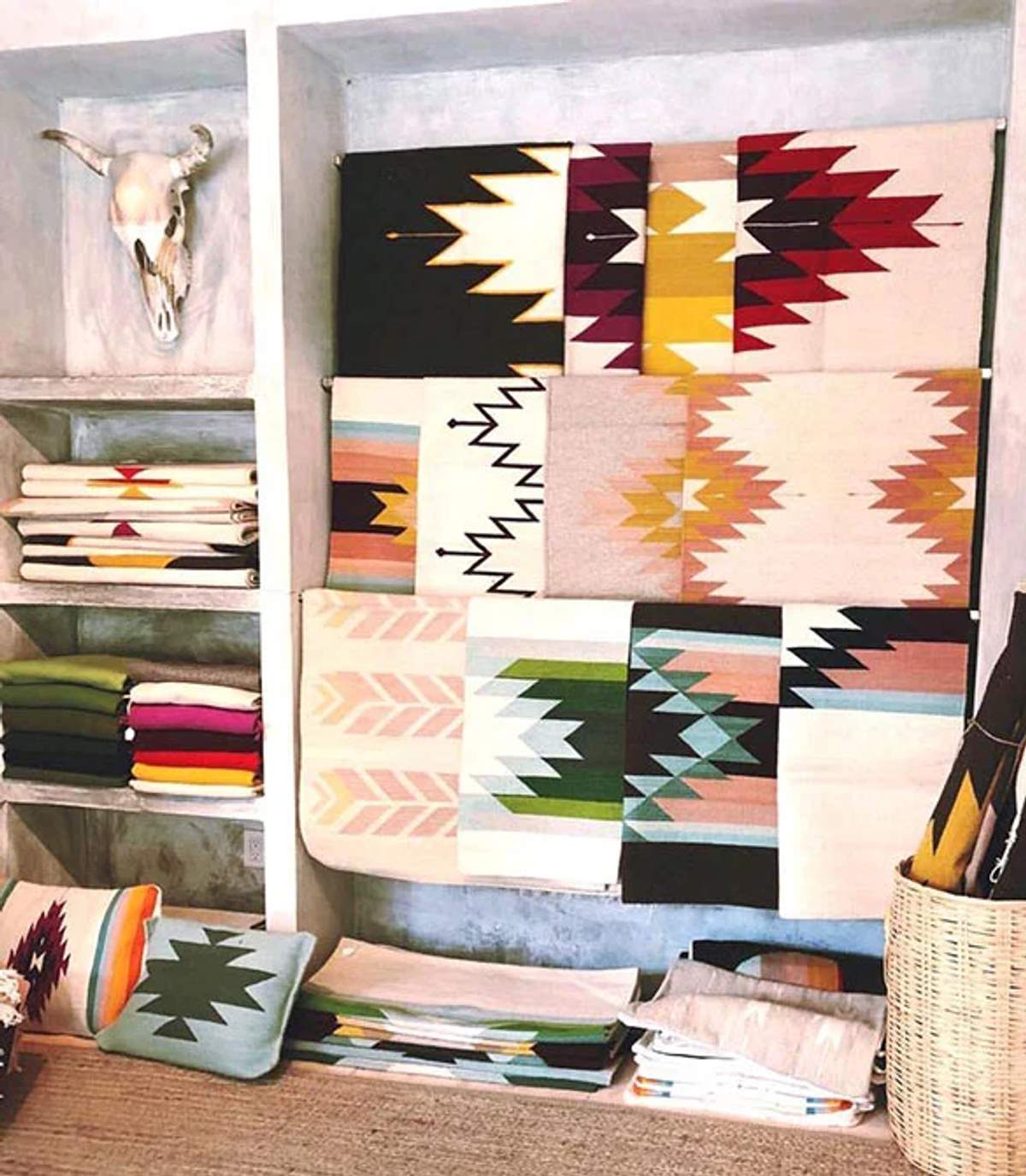 Estantes y percheros con coloridas mantas y textiles estampados, con una calavera decorativa montada en la pared.