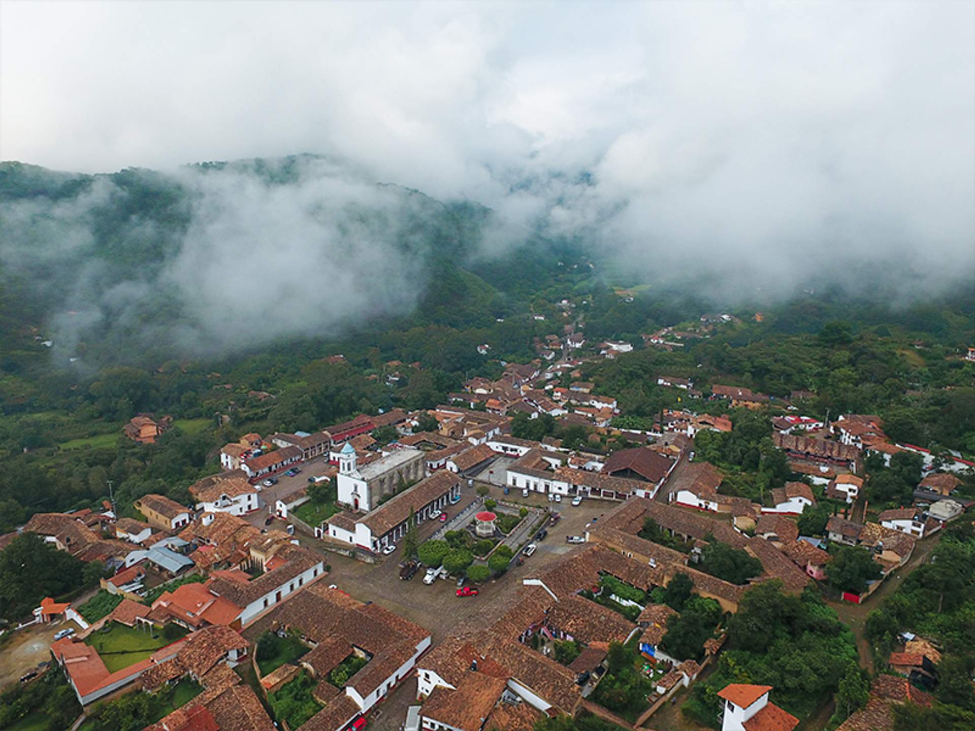 Vista aérea de un pintoresco pueblo con tejados rojos, rodeado de montañas y cubierto de neblina, en San Sebastián del Oeste