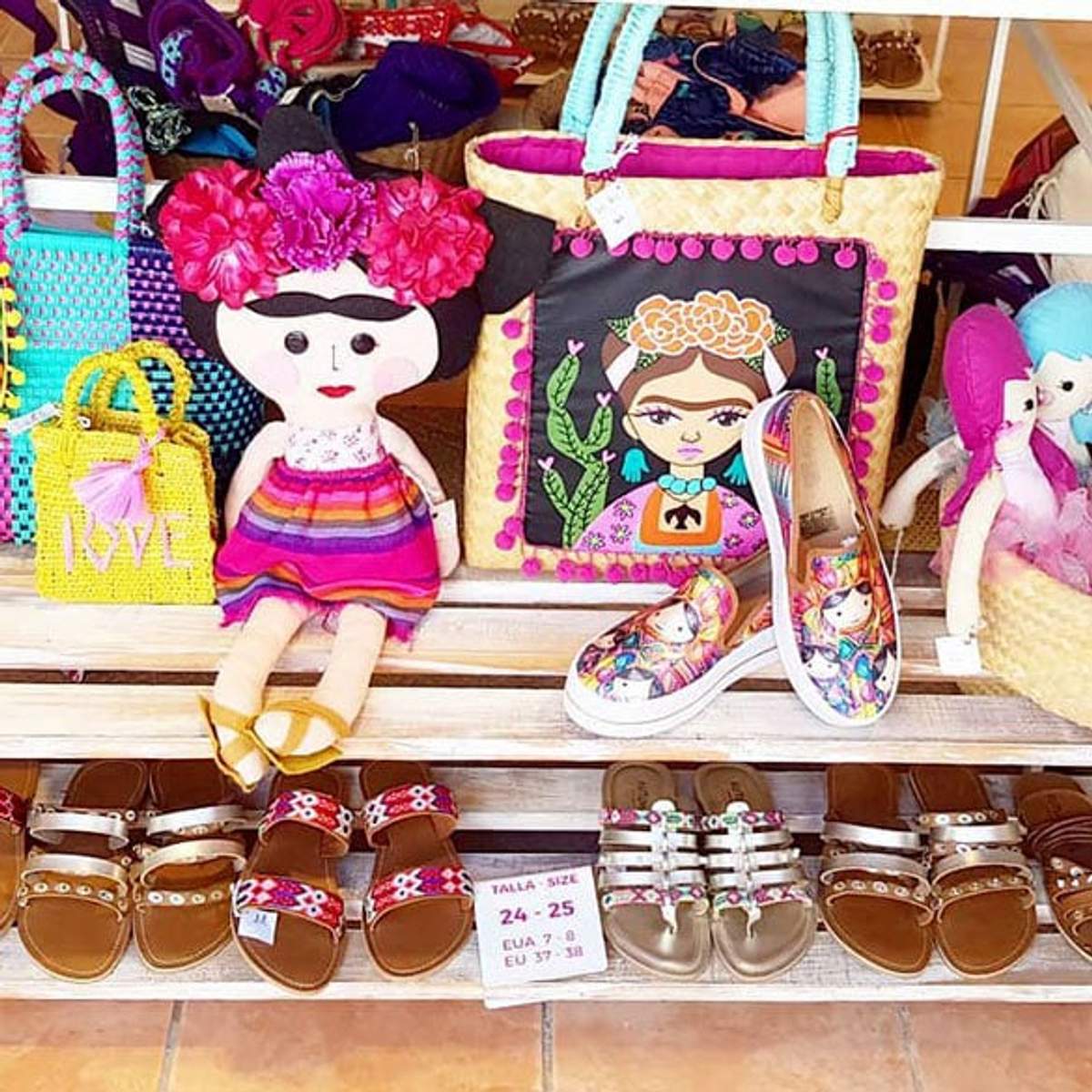 Exhibición colorida de muñecas, bolsas y zapatos en una boutique, con diseños de Frida Kahlo y varios tipos de sandalias.