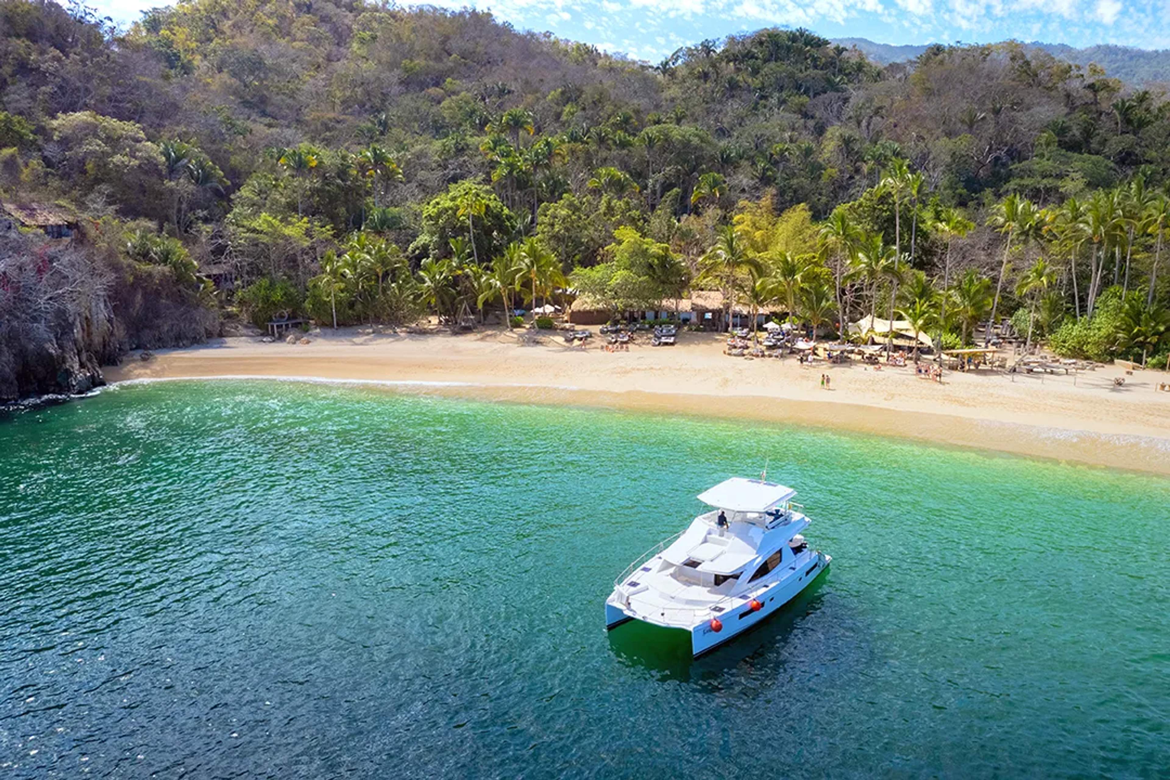 Yacht anchored near a tropical beach surrounded by lush forest.