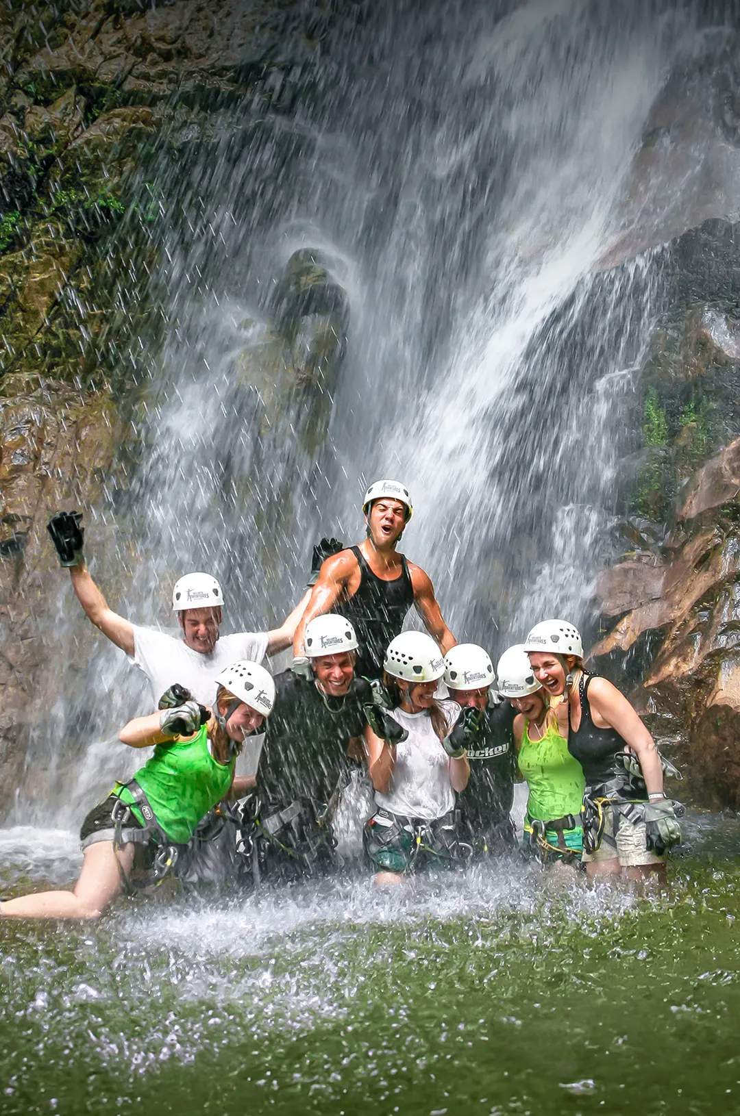 Friends equiped with helmets and harnesses enjoy standing under a waterfall in Puerto Vallarta during Outdoor Adventure.