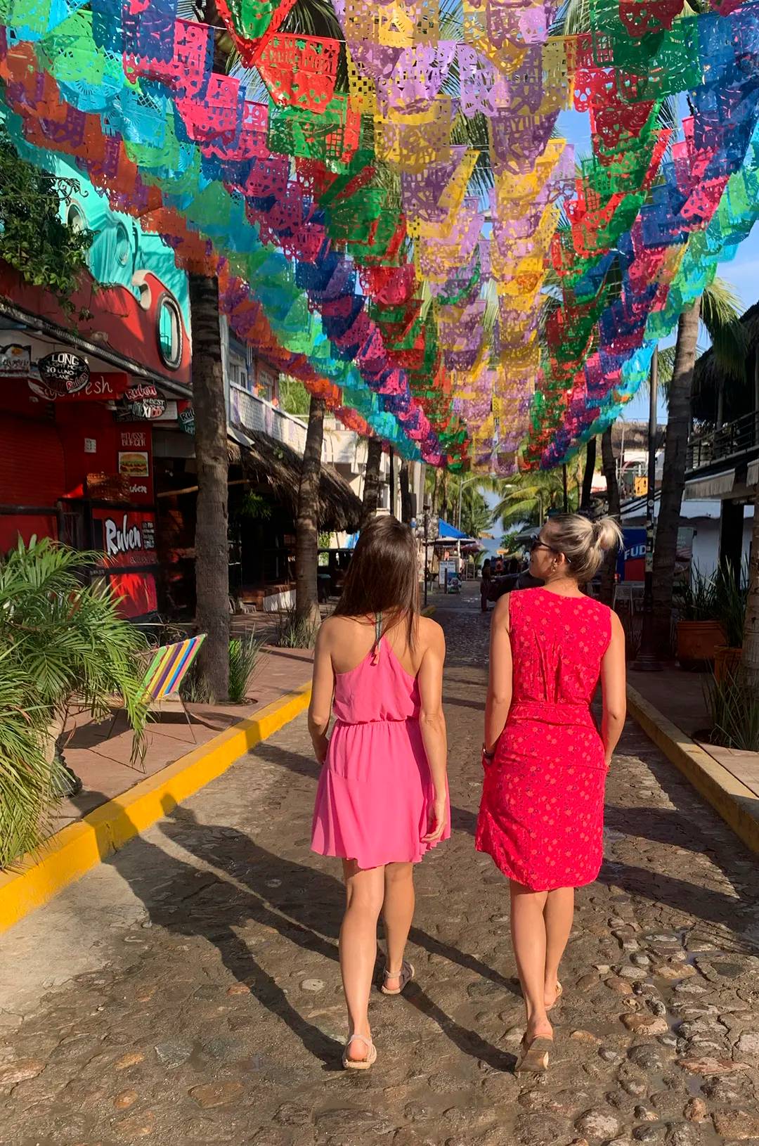 Two women walking under colorful papel picado banners in Sayulita, Mexico, during a Sayulita walking tour.