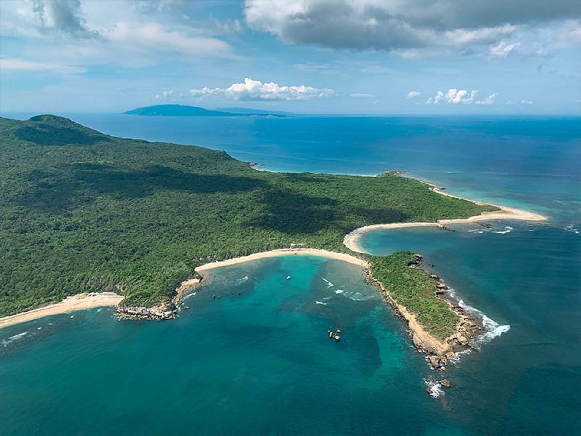 Vista aérea de una isla verde y frondosa rodeada de agua turquesa y playas de arena.