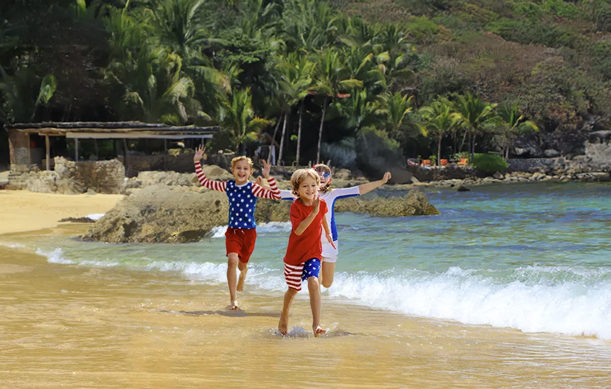 Niños corriendo y jugando en la orilla de una playa de Vallarta, vestidos con ropa de 4 de Julio.