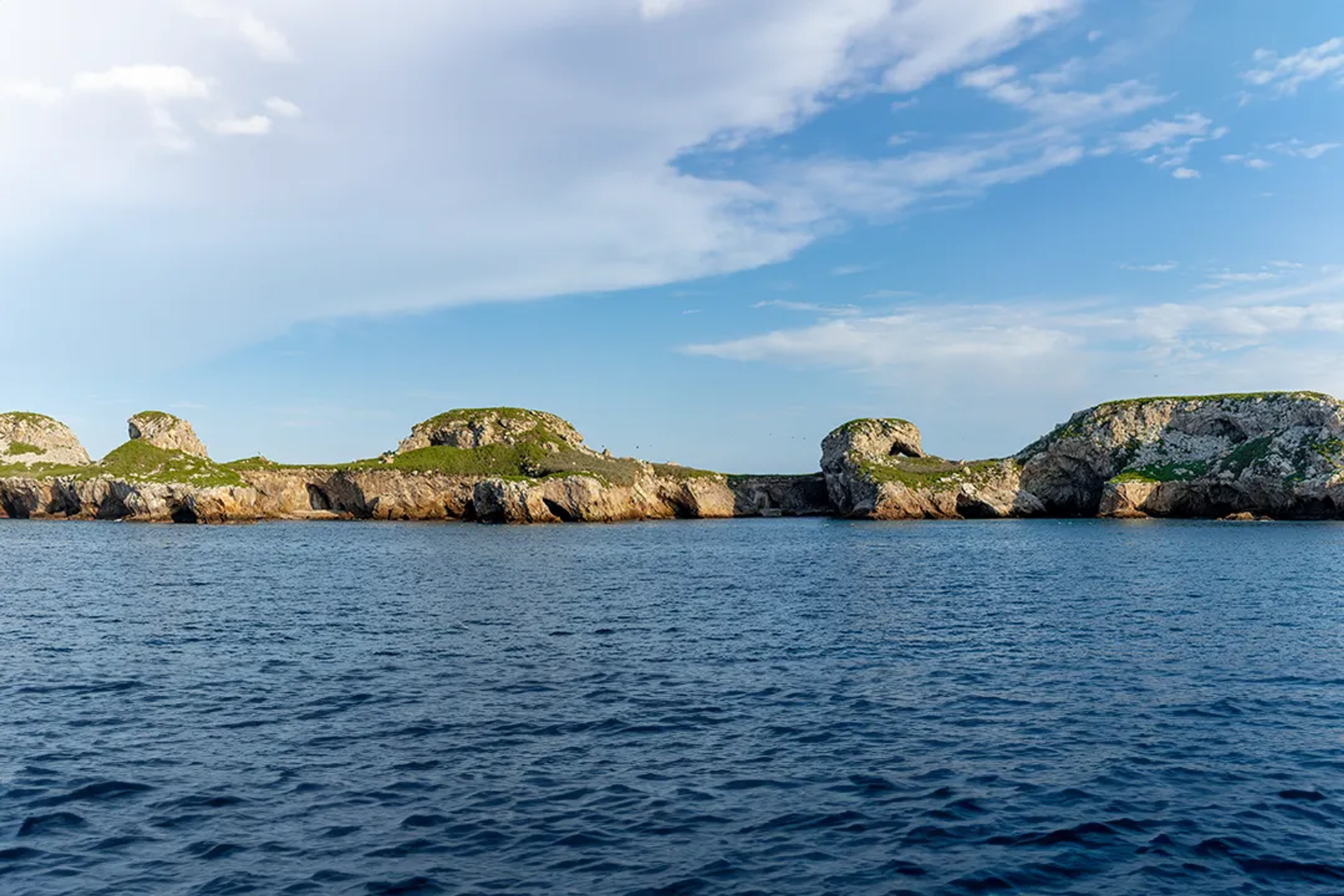 Vista de una isla rocosa con aves volando sobre ella en un cielo azul claro.