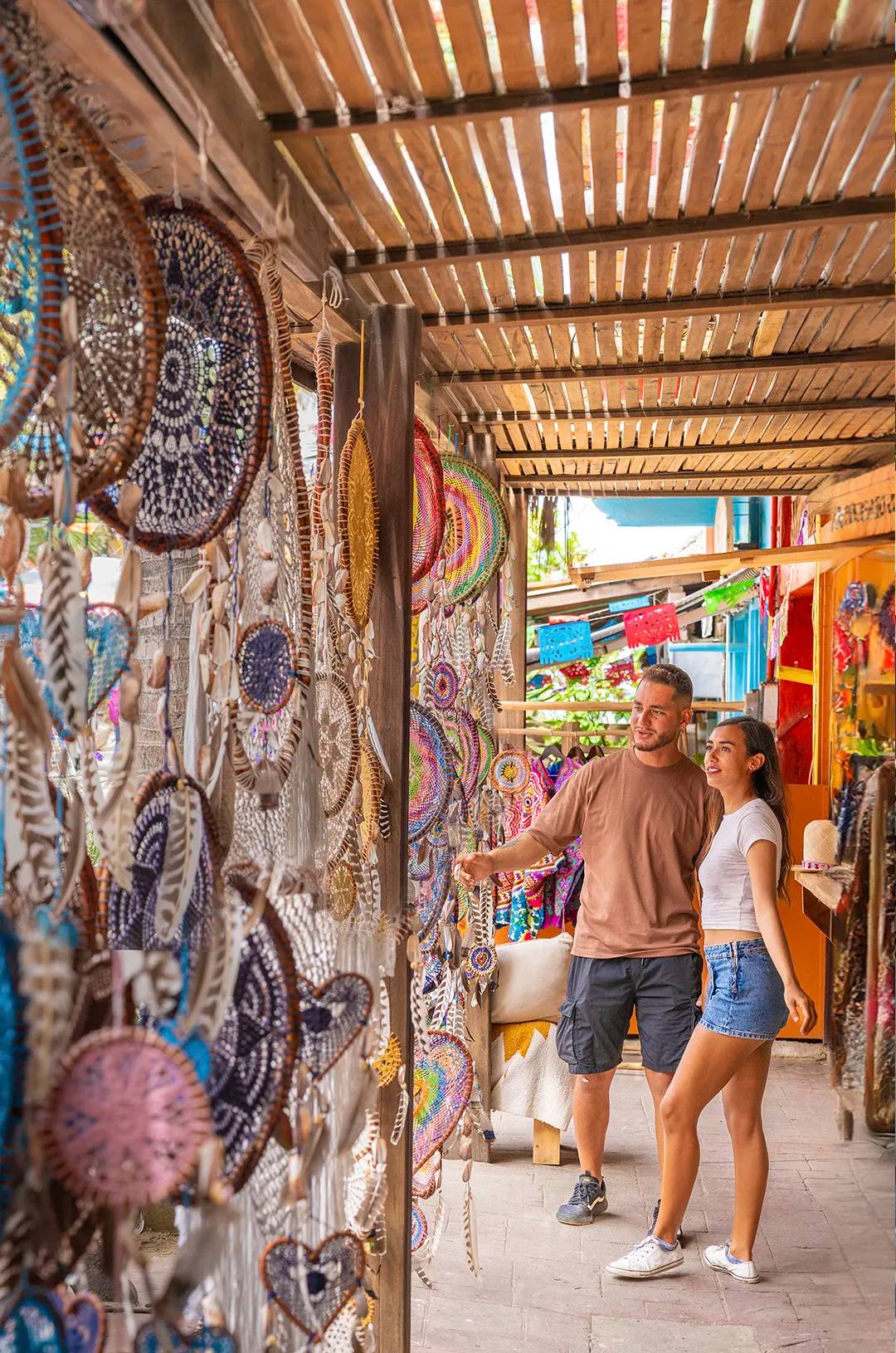 A couple browsing colorful dreamcatchers at a market stall in Sayulita.
