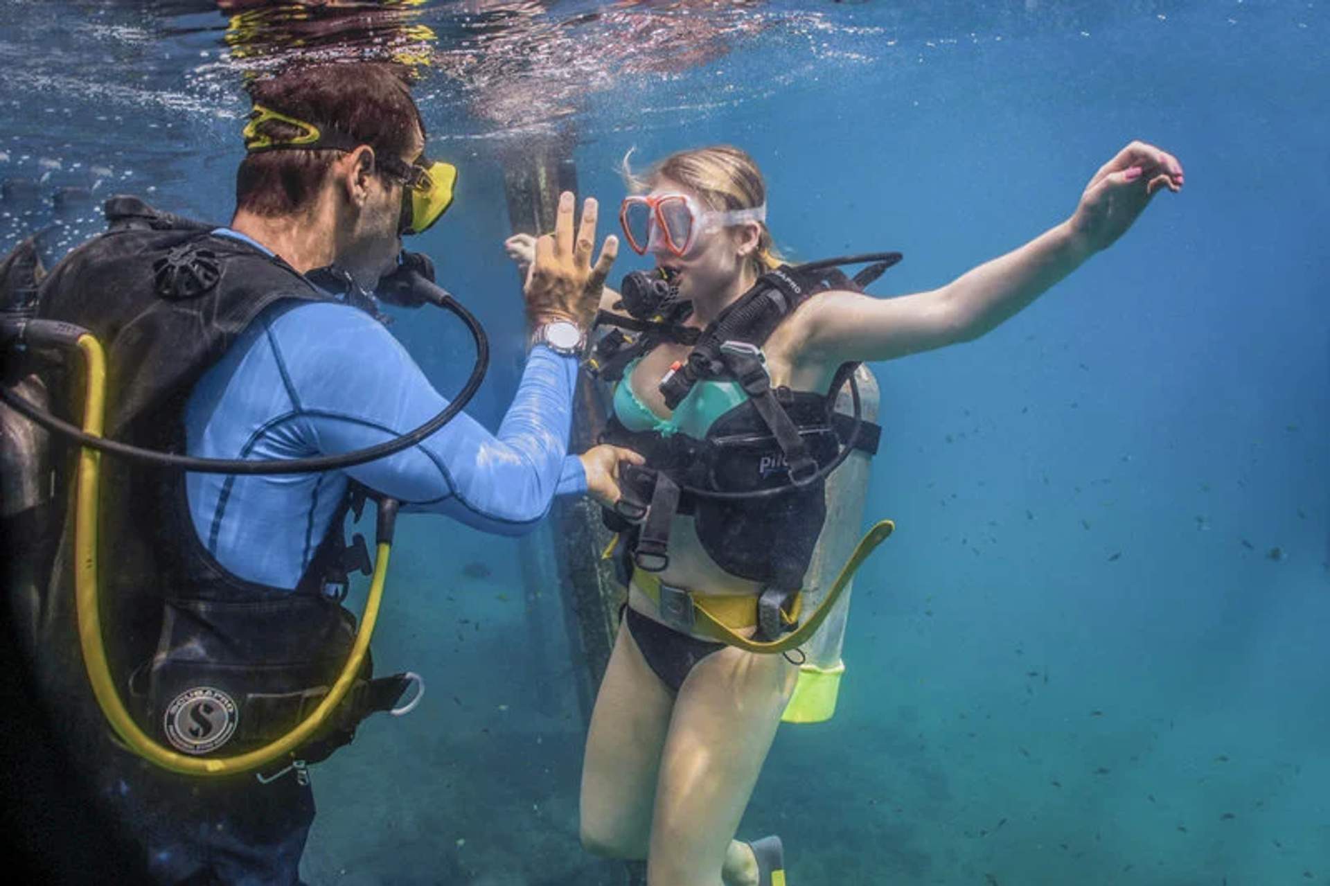 Un instructor de buceo enseña a una mujer bajo el agua en Puerto Vallarta, usando señales de mano para comunicarse.
