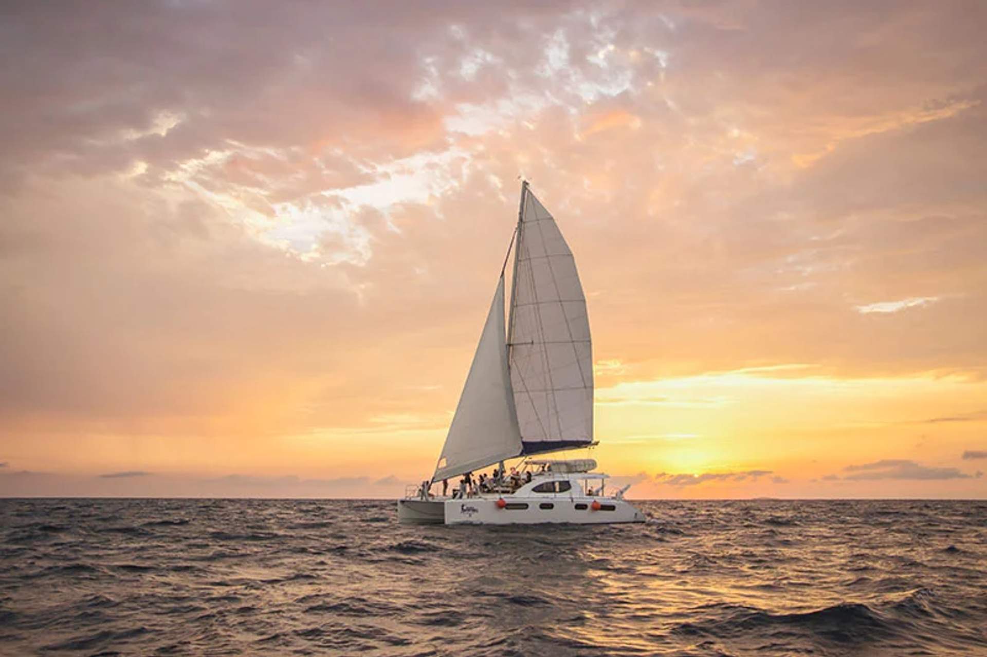 Un velero navega por el océano al atardecer, con un cielo impresionante lleno de tonos naranjas y rosas.