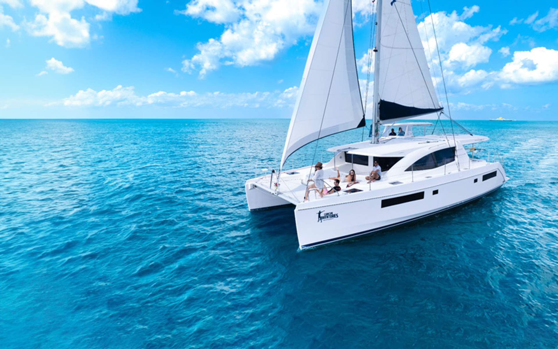 Catamaran sailing on clear blue waters with people on deck.