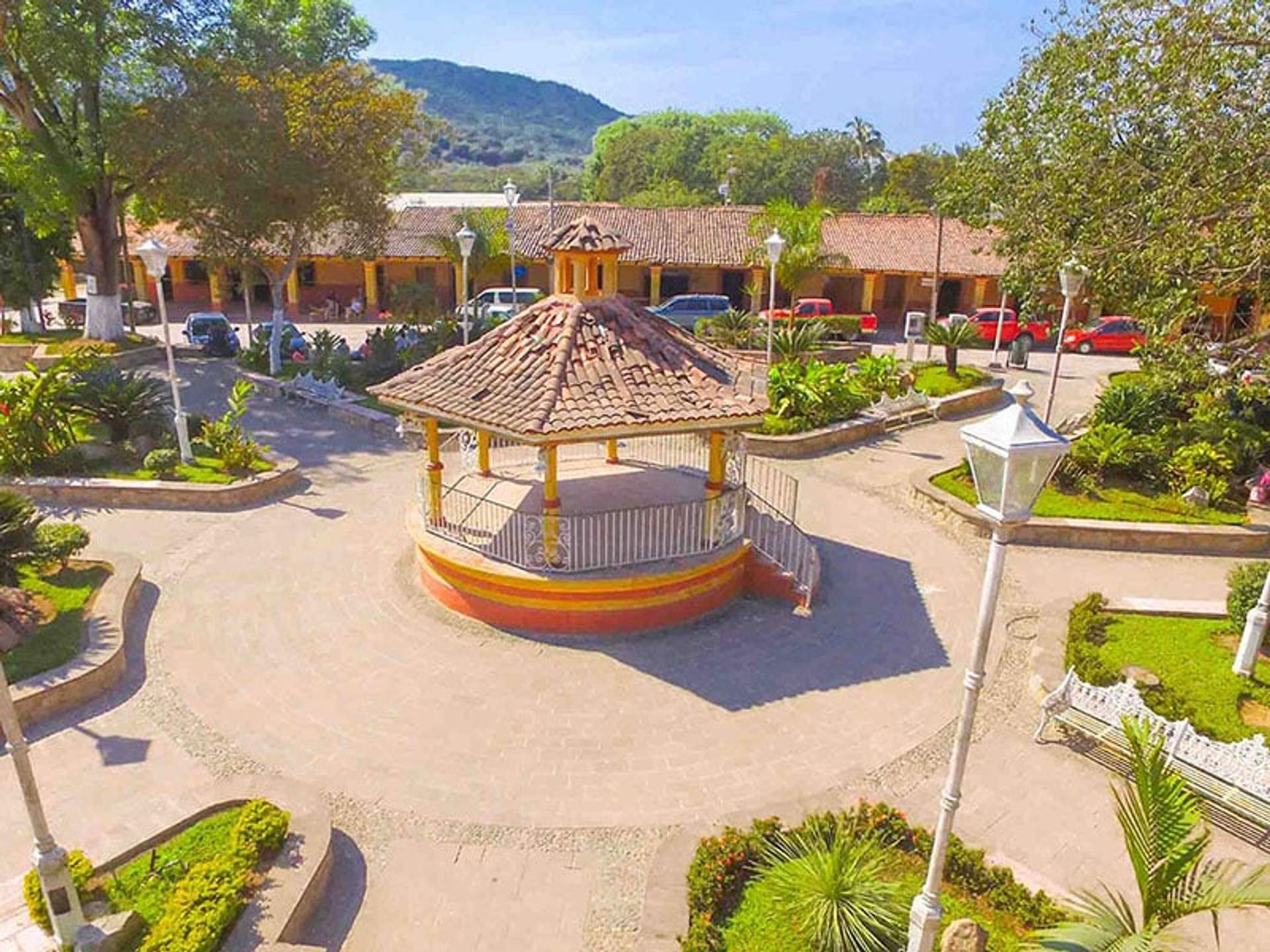 A charming gazebo in the center of a town square surrounded by lush greenery and colonial-style buildings.