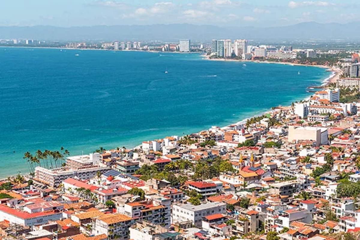 Aerial view of Puerto Vallarta's coastline, showcasing the city's buildings and the blue ocean stretching into the distance.